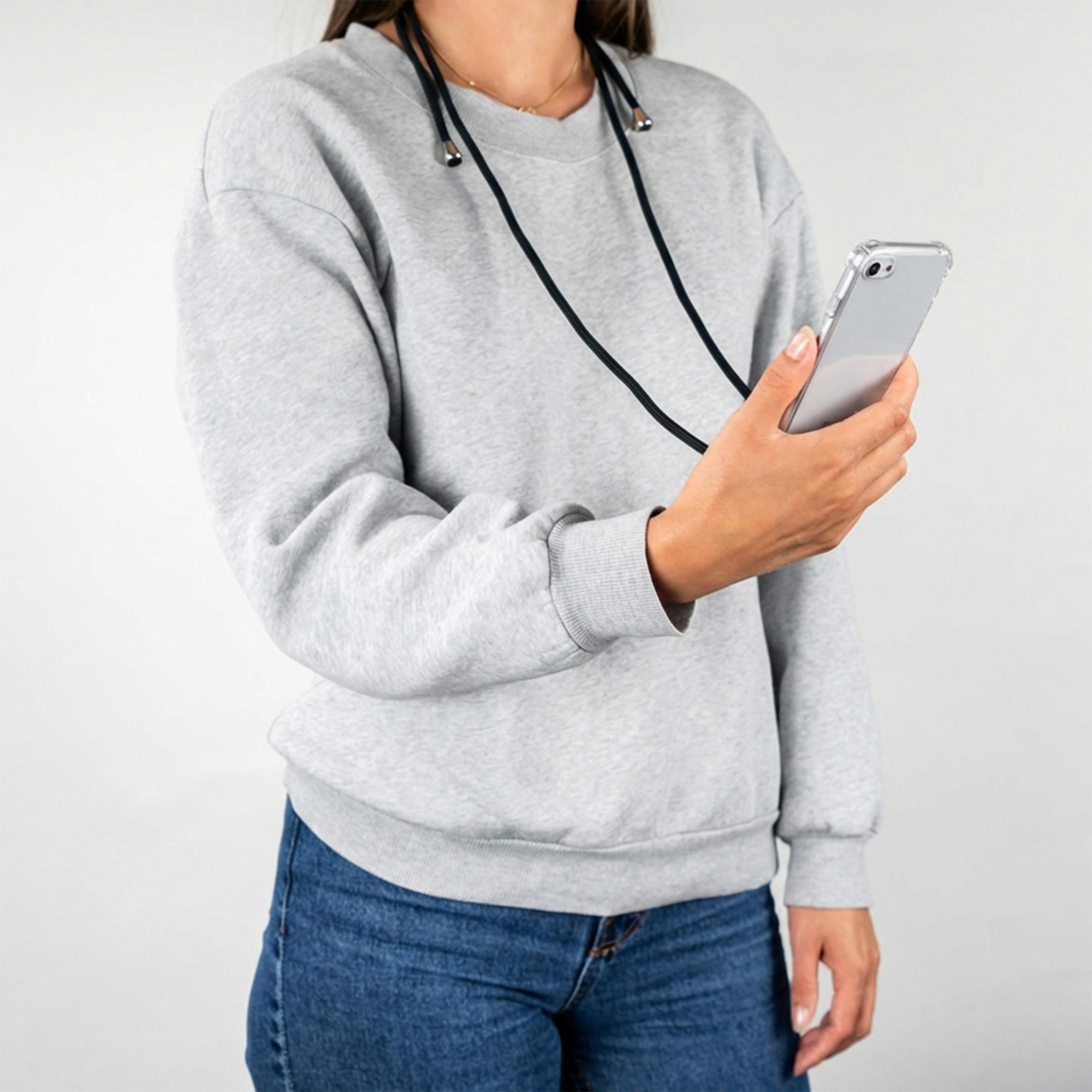 Una donna con felpa grigia e jeans blu tiene uno smartphone con cordino su sfondo bianco.