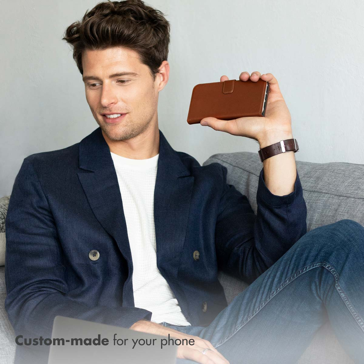 Un homme souriant assis sur un canapé tient une coque de téléphone marron.