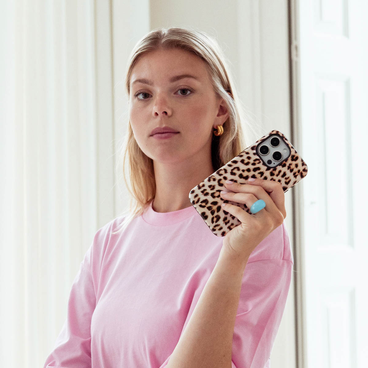 Una donna bionda con una maglietta rosa tiene in mano un telefono leopardato e indossa un anello blu.
