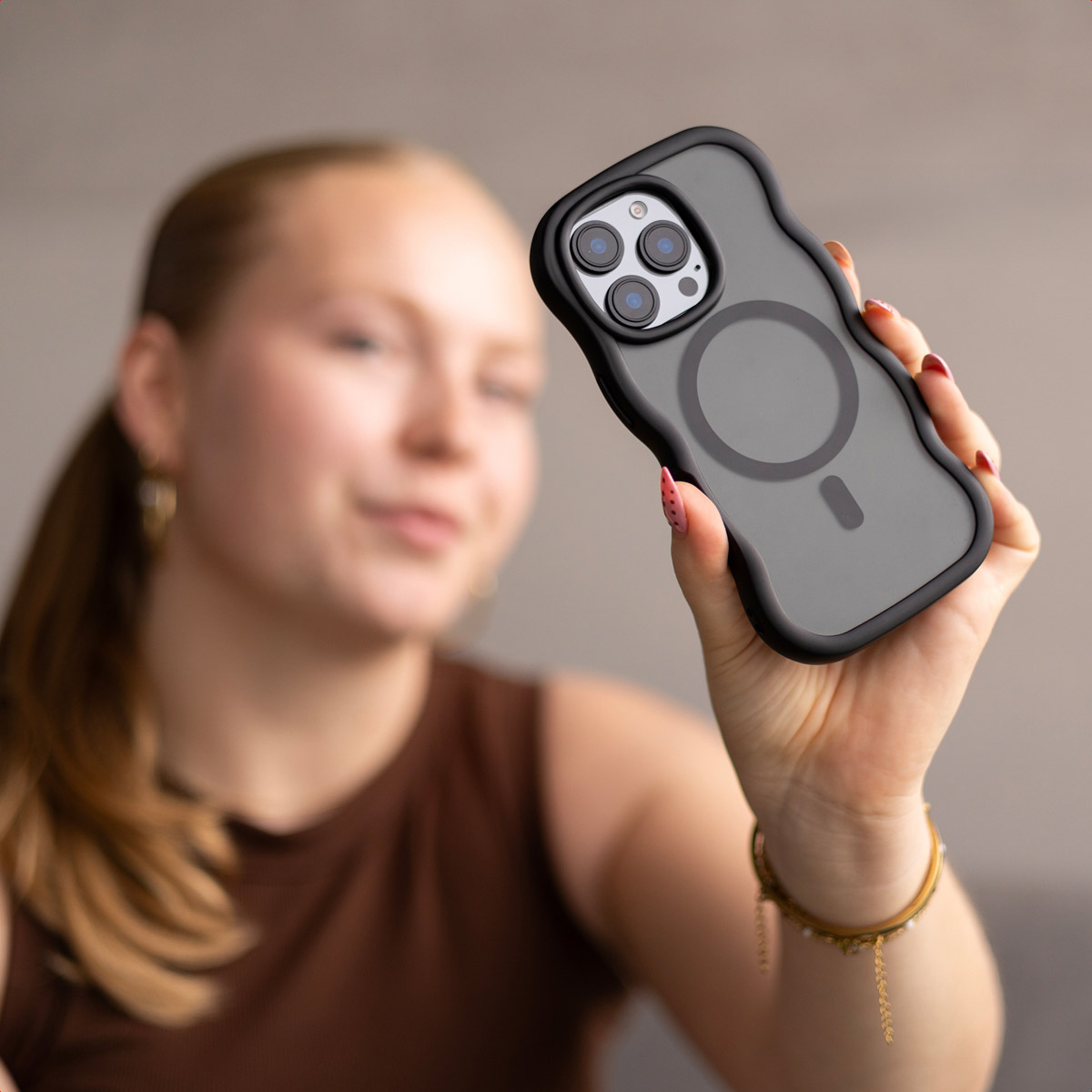 Una mujer sostiene una funda de smartphone negra y ondulada hacia la cámara mientras sonríe levemente.