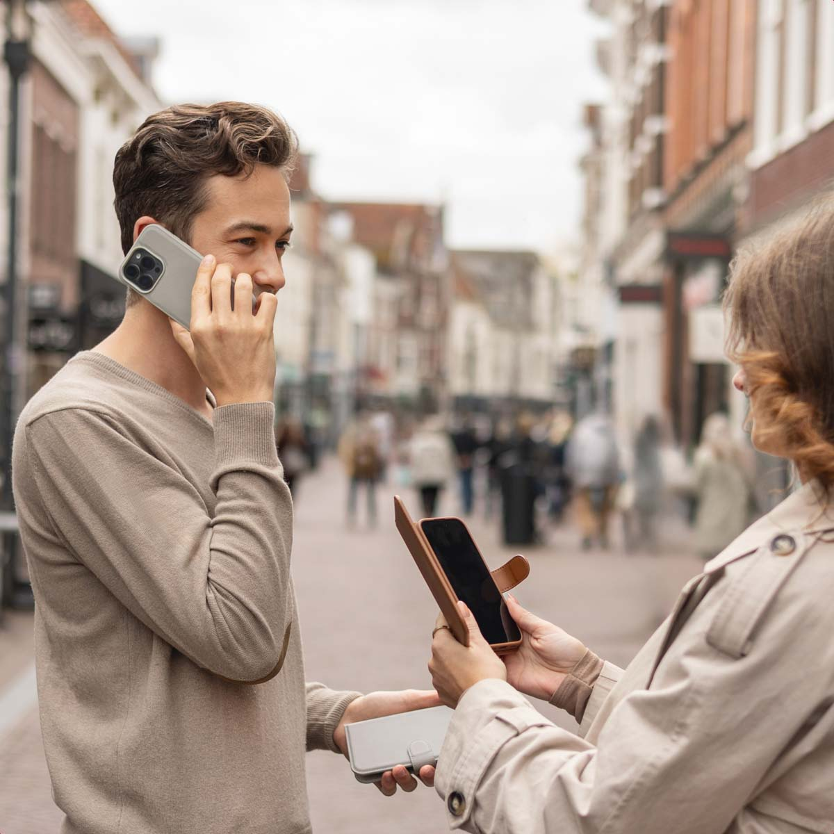 Un hombre habla por teléfono en la calle mientras una mujer le muestra un smartphone en una funda.