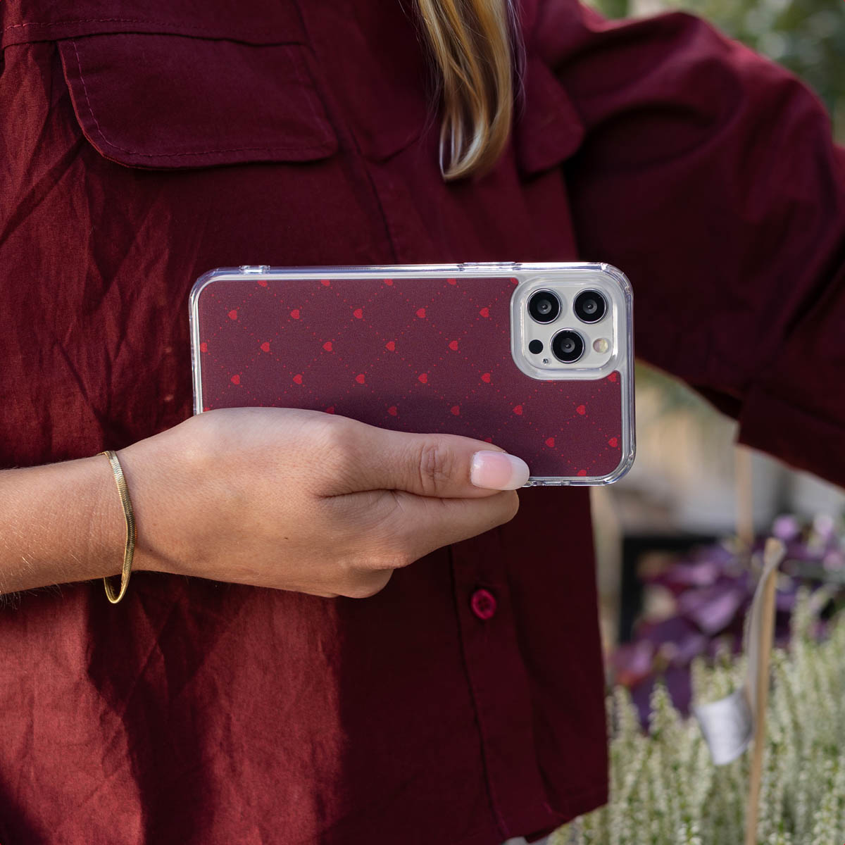 Une personne en chemise rouge tient un smartphone à coque avec des cœurs.