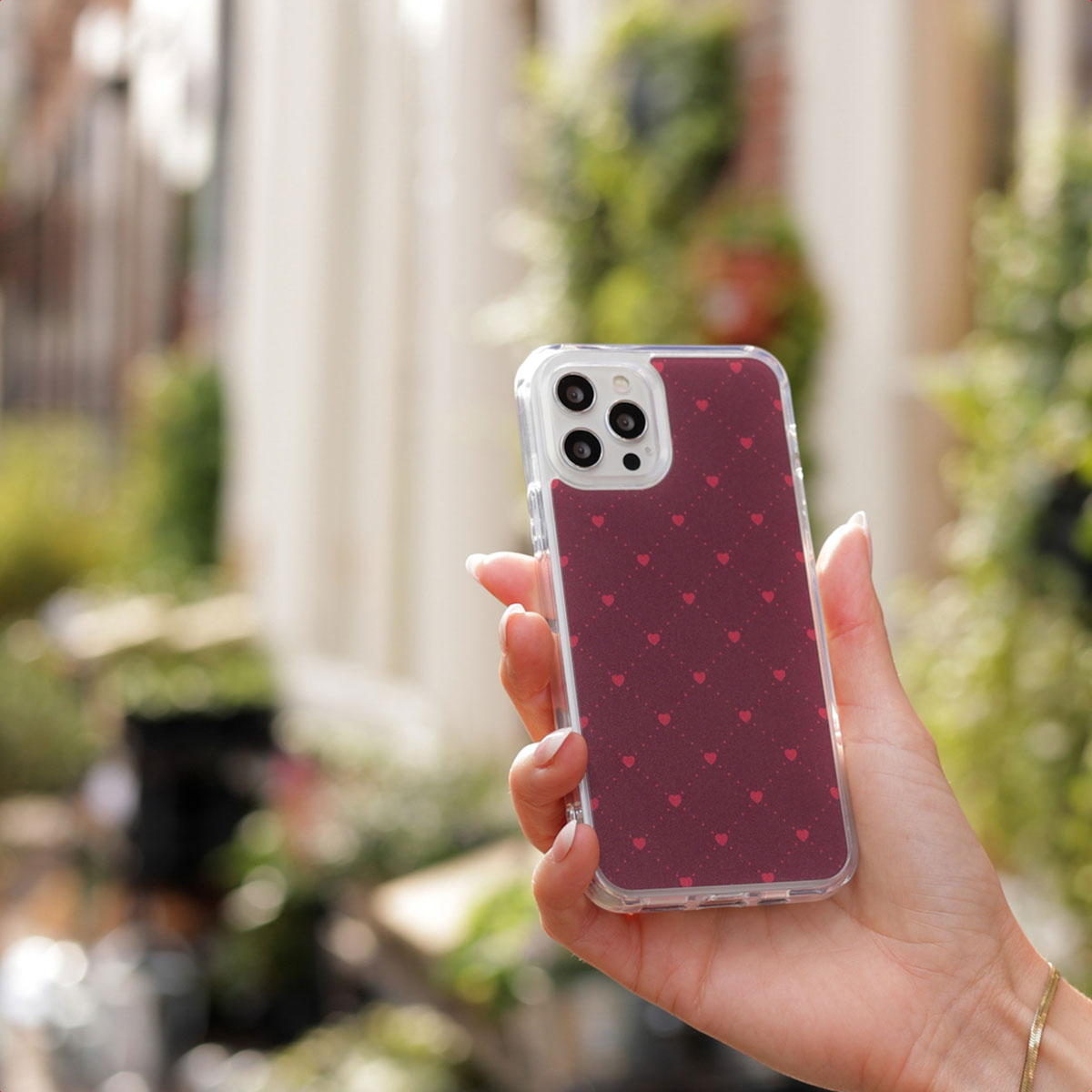 Main tenant un smartphone rouge avec motif de cœurs et coque de protection.