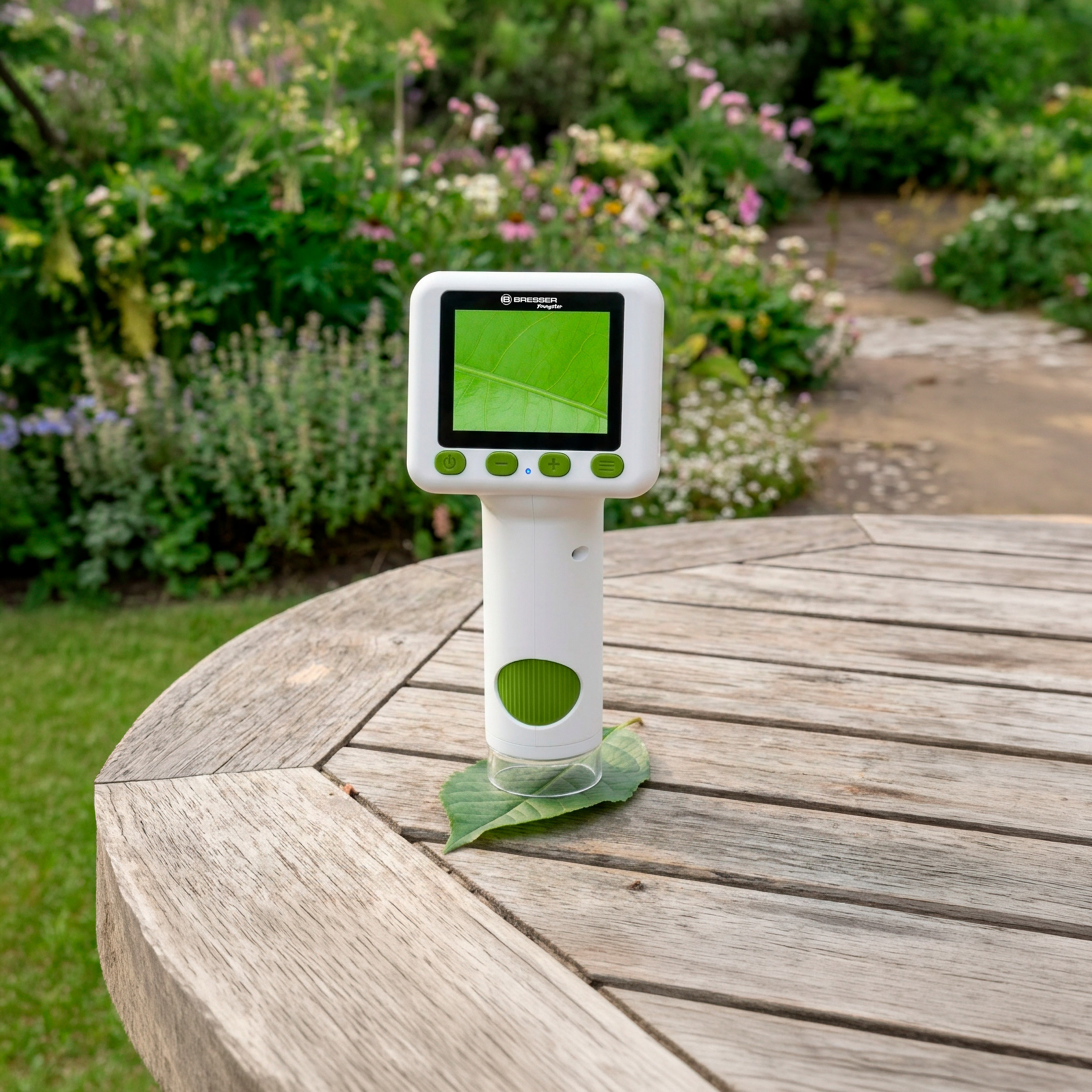 Un microscopio digital blanco está sobre una mesa de madera en un jardín, observando una hoja verde.