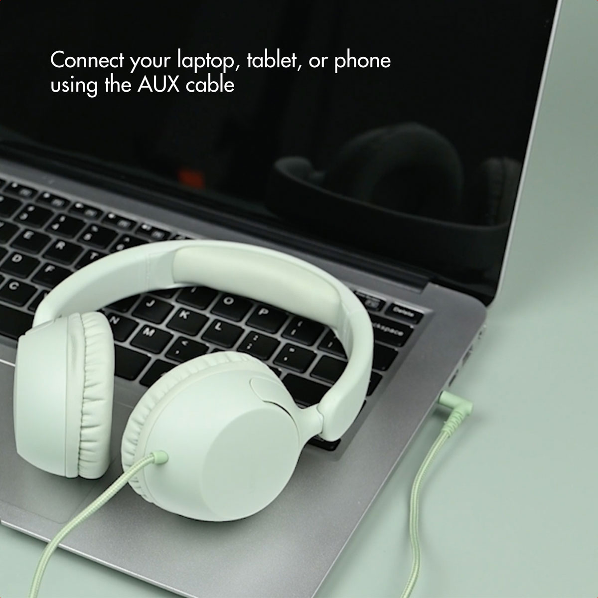 Auriculares verde claro descansan sobre el teclado de una computadora portátil. Un cable de audio está conectado a ellos.