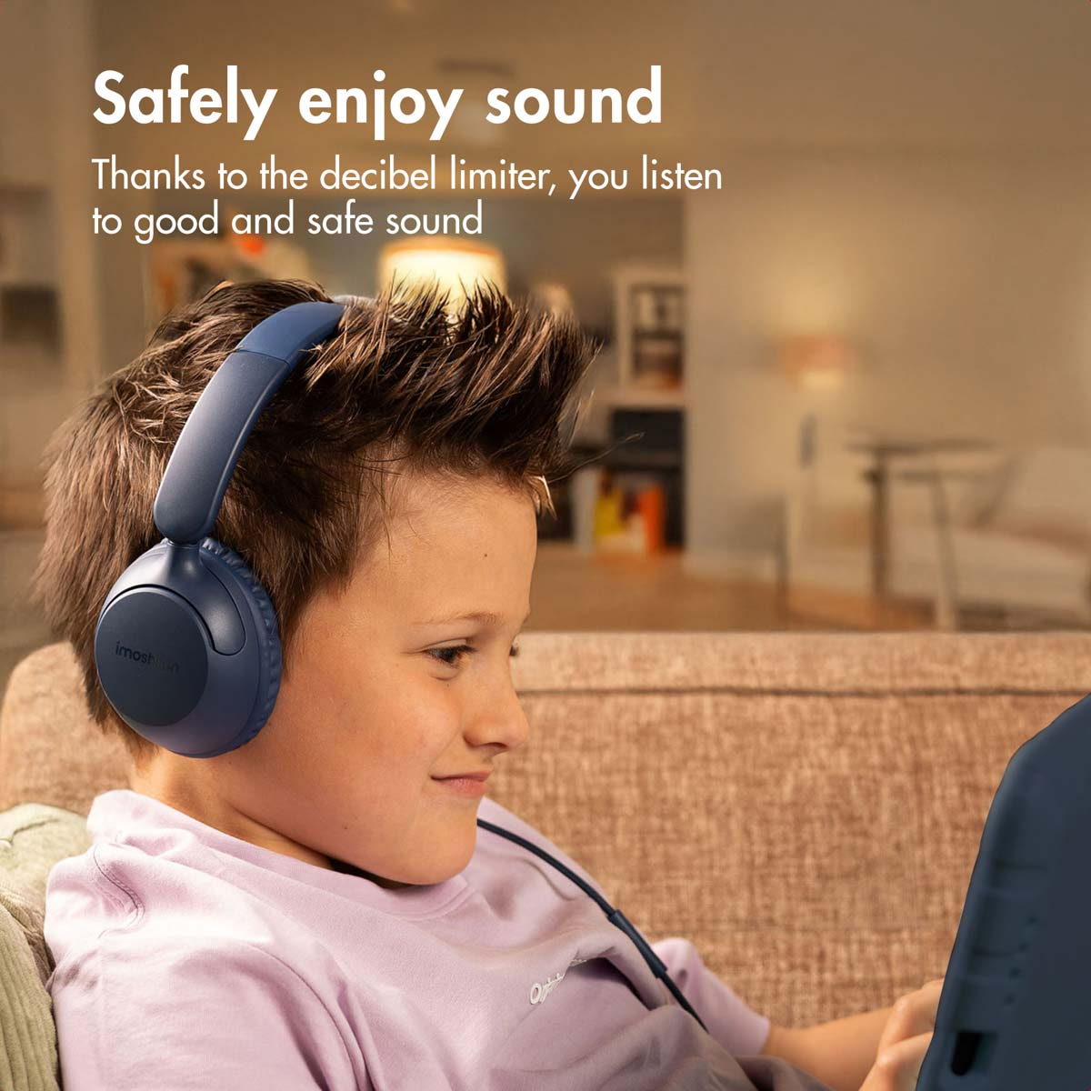 Un niño con auriculares azules está sentado en un sofá mirando una tableta.