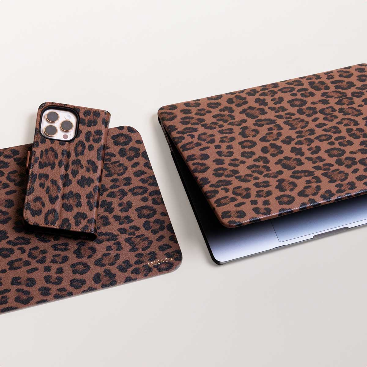 Una computadora portátil, un teléfono con funda y una alfombrilla con estampado de leopardo marrón.