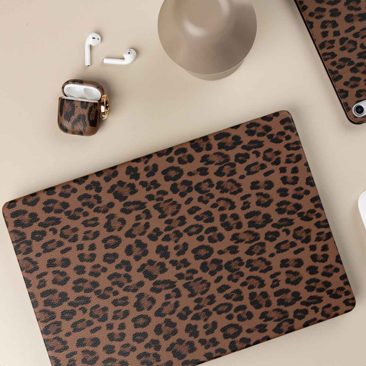 Portátil, auriculares y taza con estampado de leopardo en mesa beige.