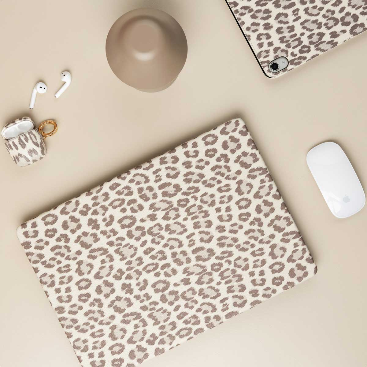 Una laptop, tableta, ratón y auriculares con estampado de leopardo sobre un escritorio beige.