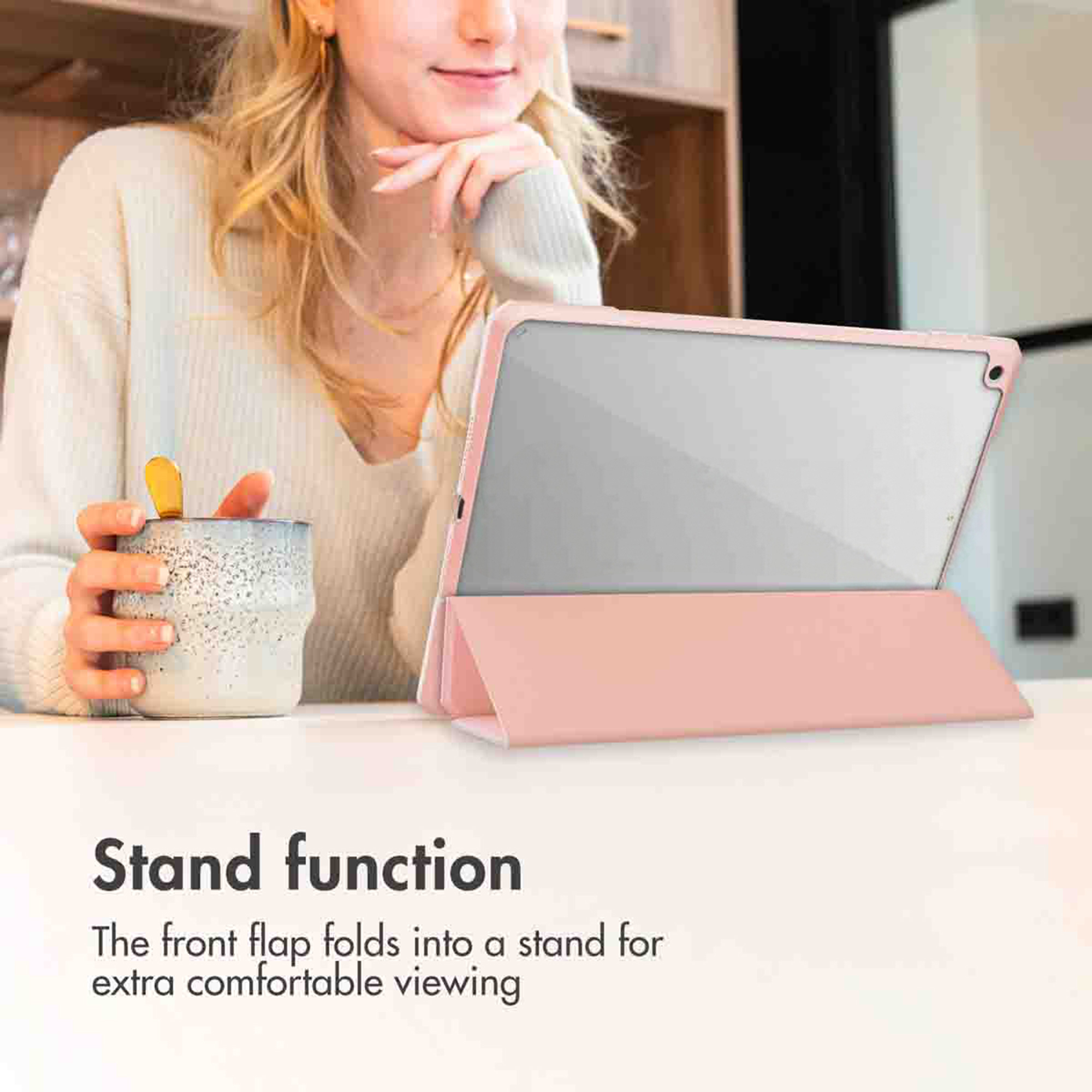 Een vrouw houdt een mok vast naast een roze tablet in standaard.