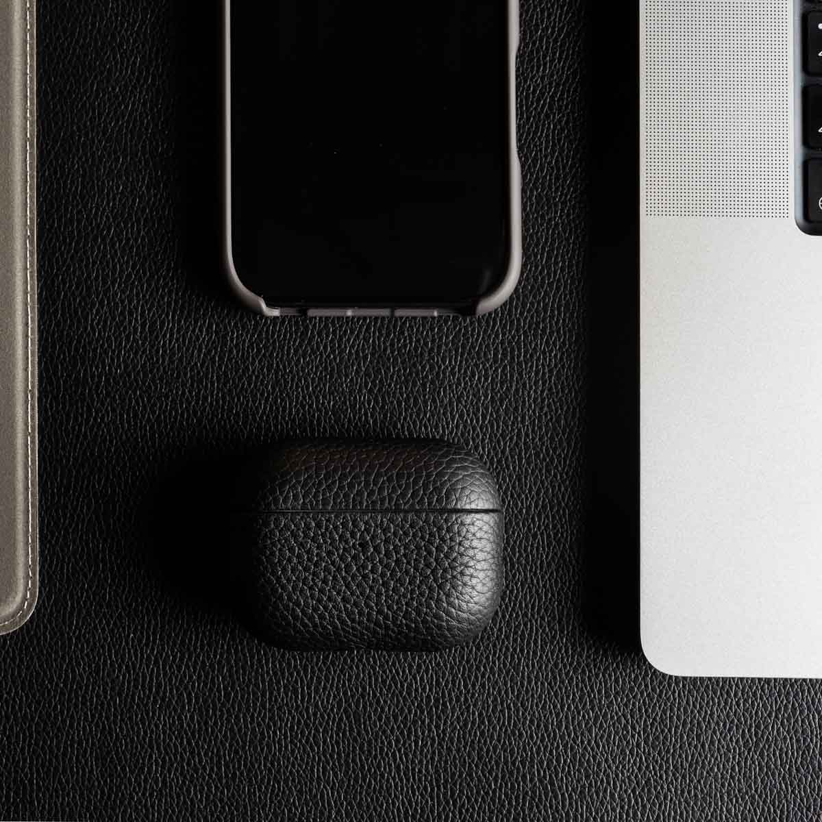 Uno smartphone, una custodia per AirPods in pelle e un laptop su pelle nera.