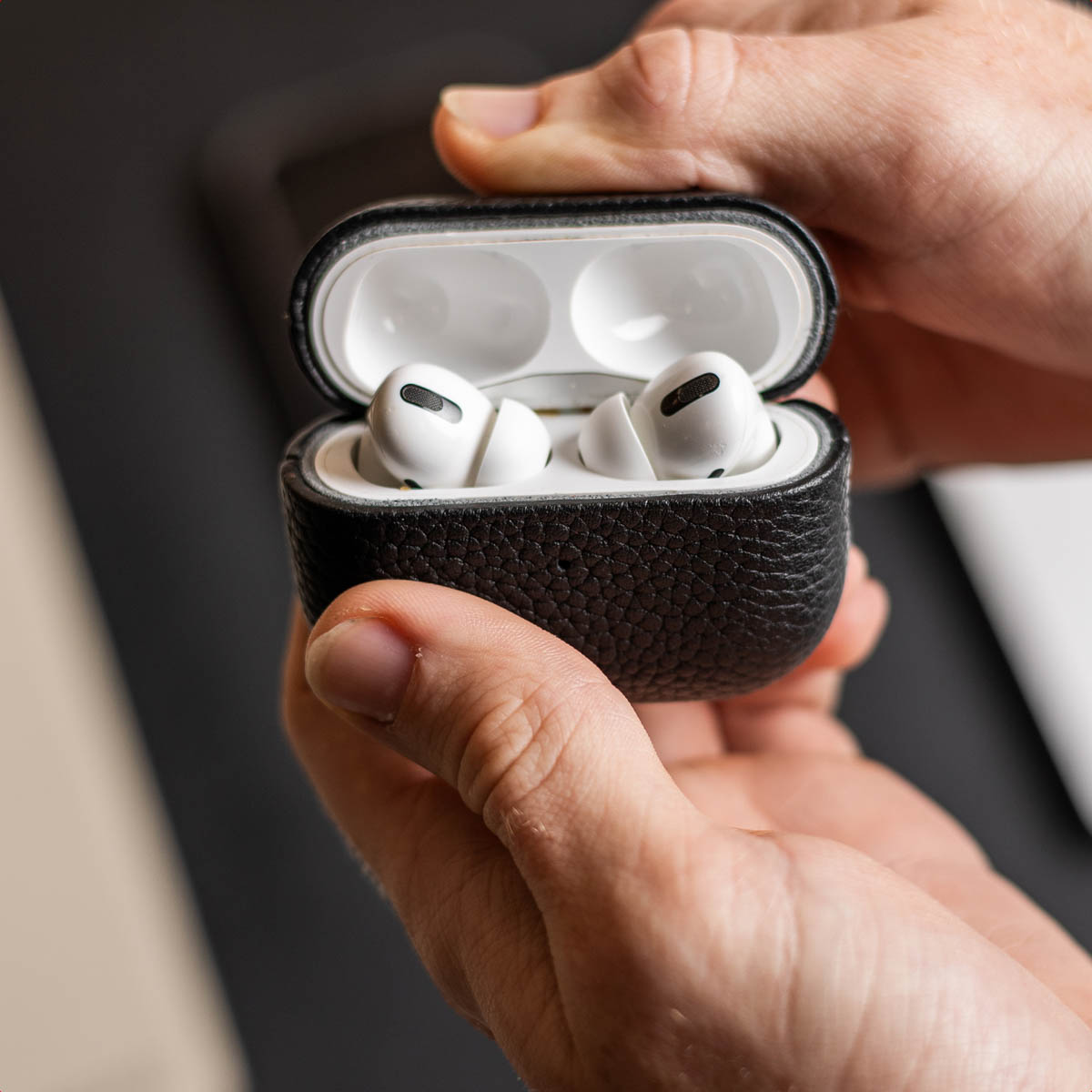 Persona che tiene aperto un astuccio in pelle nera contenente due auricolari wireless bianchi.