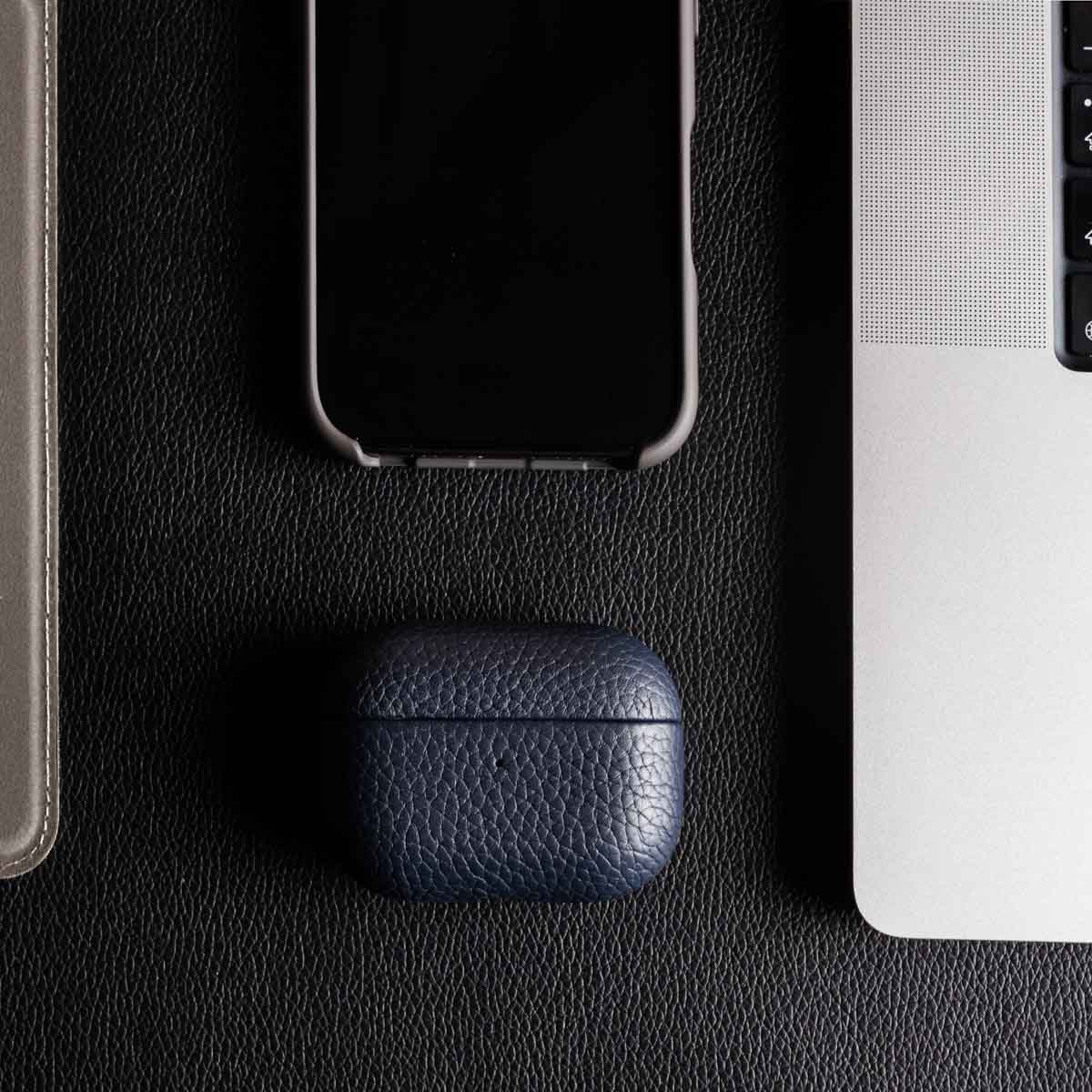 Uno smartphone, una custodia per cuffie in pelle blu e un computer portatile su una scrivania nera.