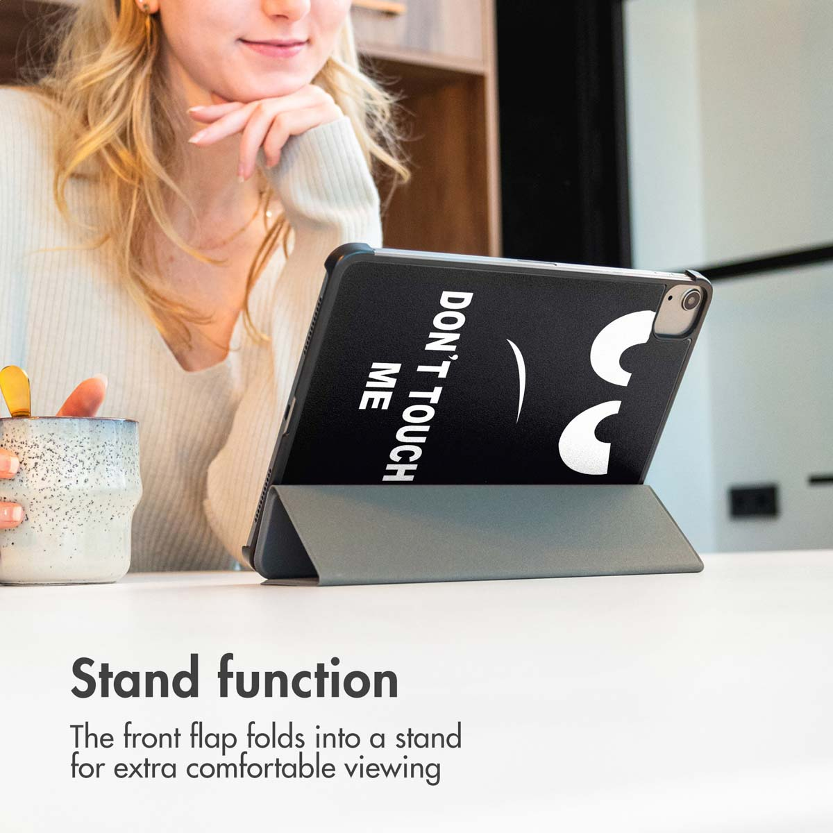 Een tablet in een beschermhoes staat op een tafel terwijl een vrouw toekijkt.
