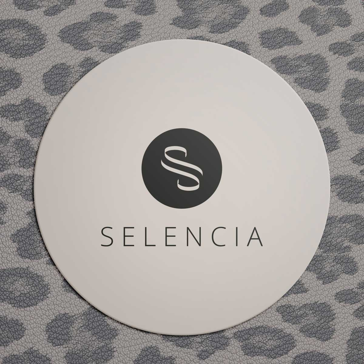 Un posavasos redondo blanco presenta el logotipo negro "SELENCIA" sobre un fondo con patrón.