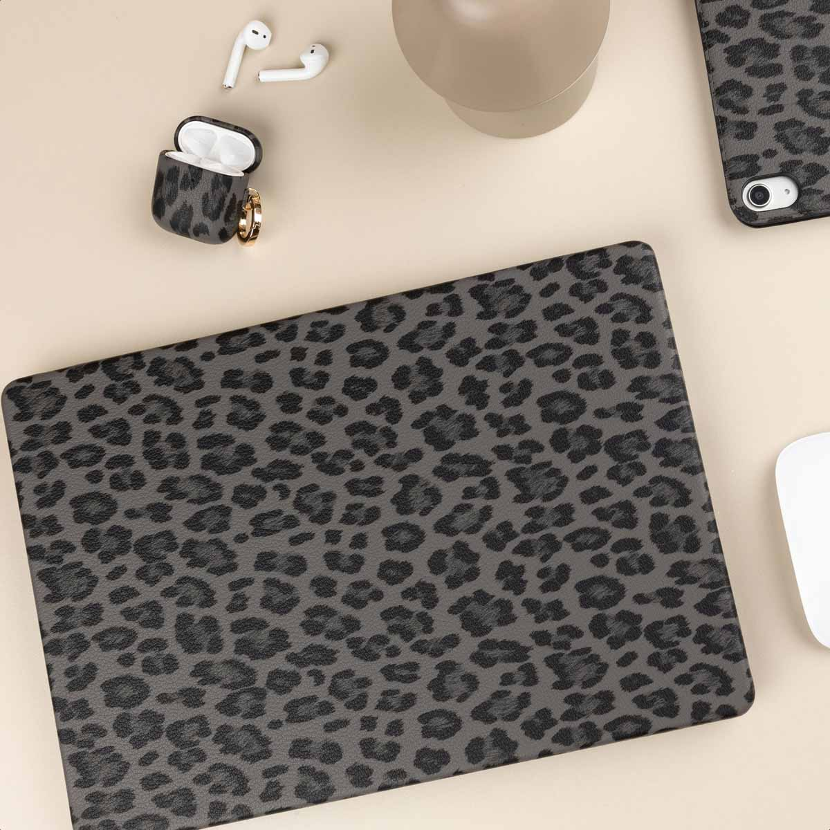 Portátil, AirPods con funda, teléfono y taza sobre mesa clara con estampado de leopardo gris.