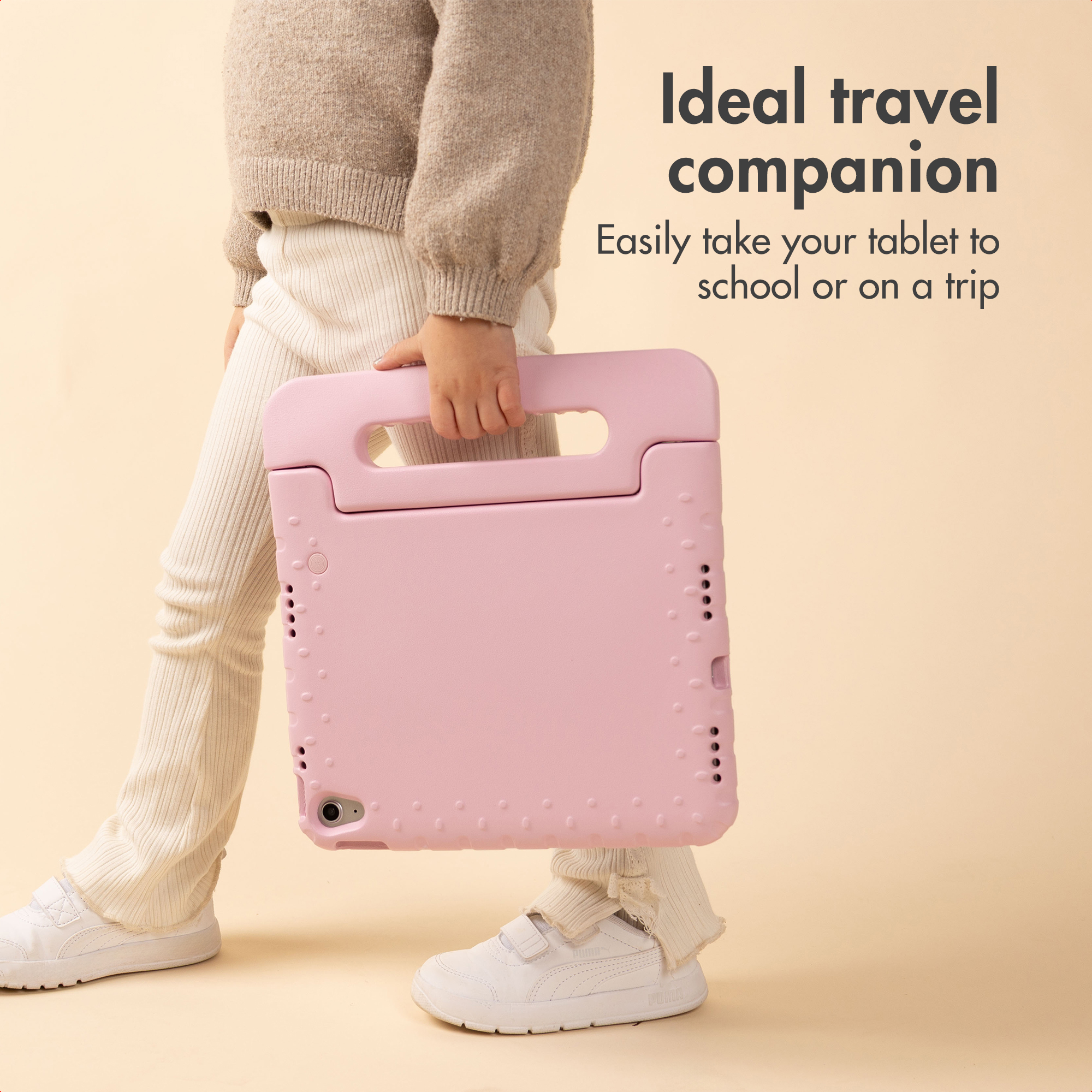 Een kind in crème kleding draagt een roze tablethoes met handvat tegen een beige achtergrond.