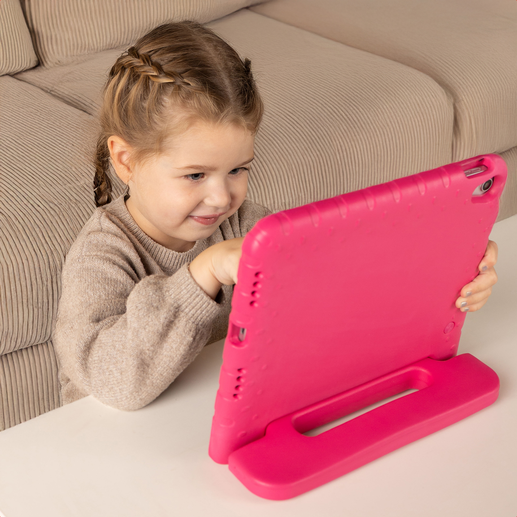 Una bambina con trecce e un maglione grigio siede davanti a una custodia per tablet rosa.