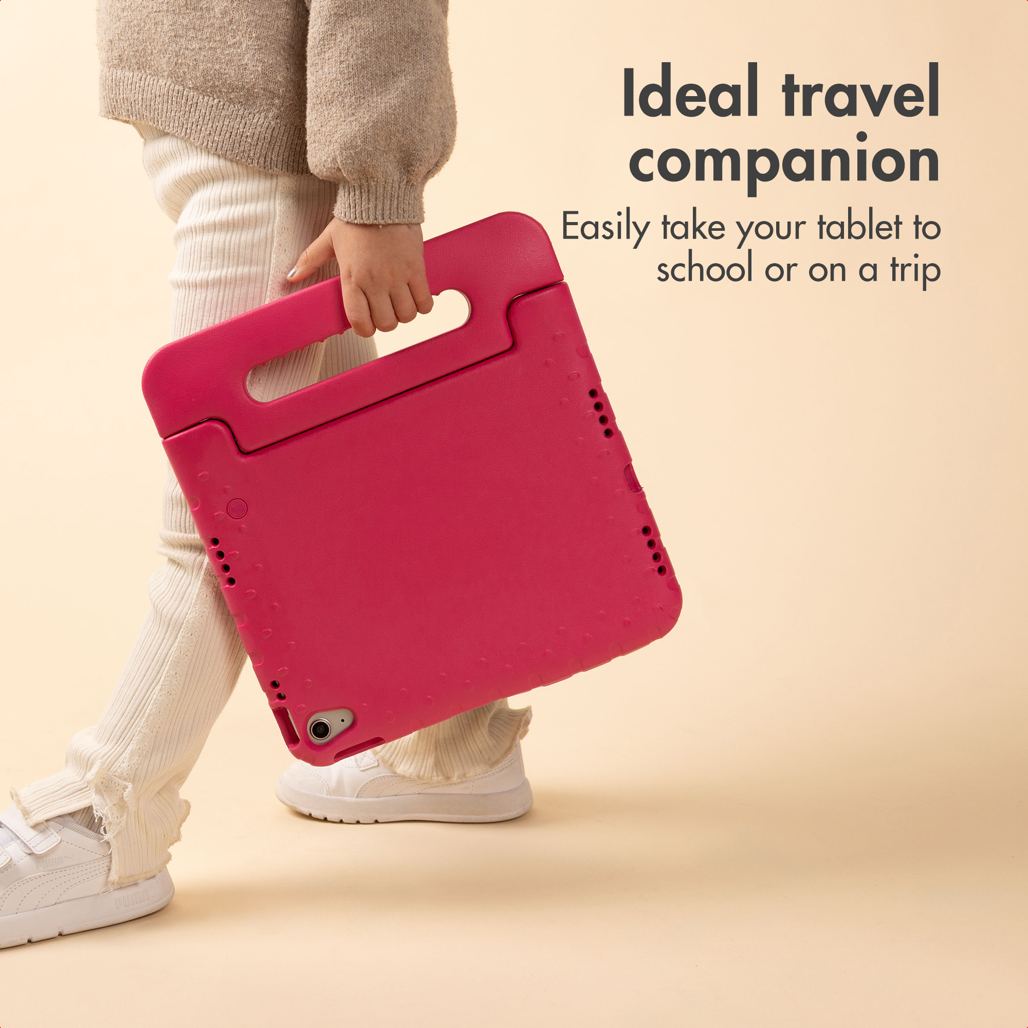 Un bambino cammina tenendo una custodia per tablet rosa vivo con maniglia su sfondo beige.
