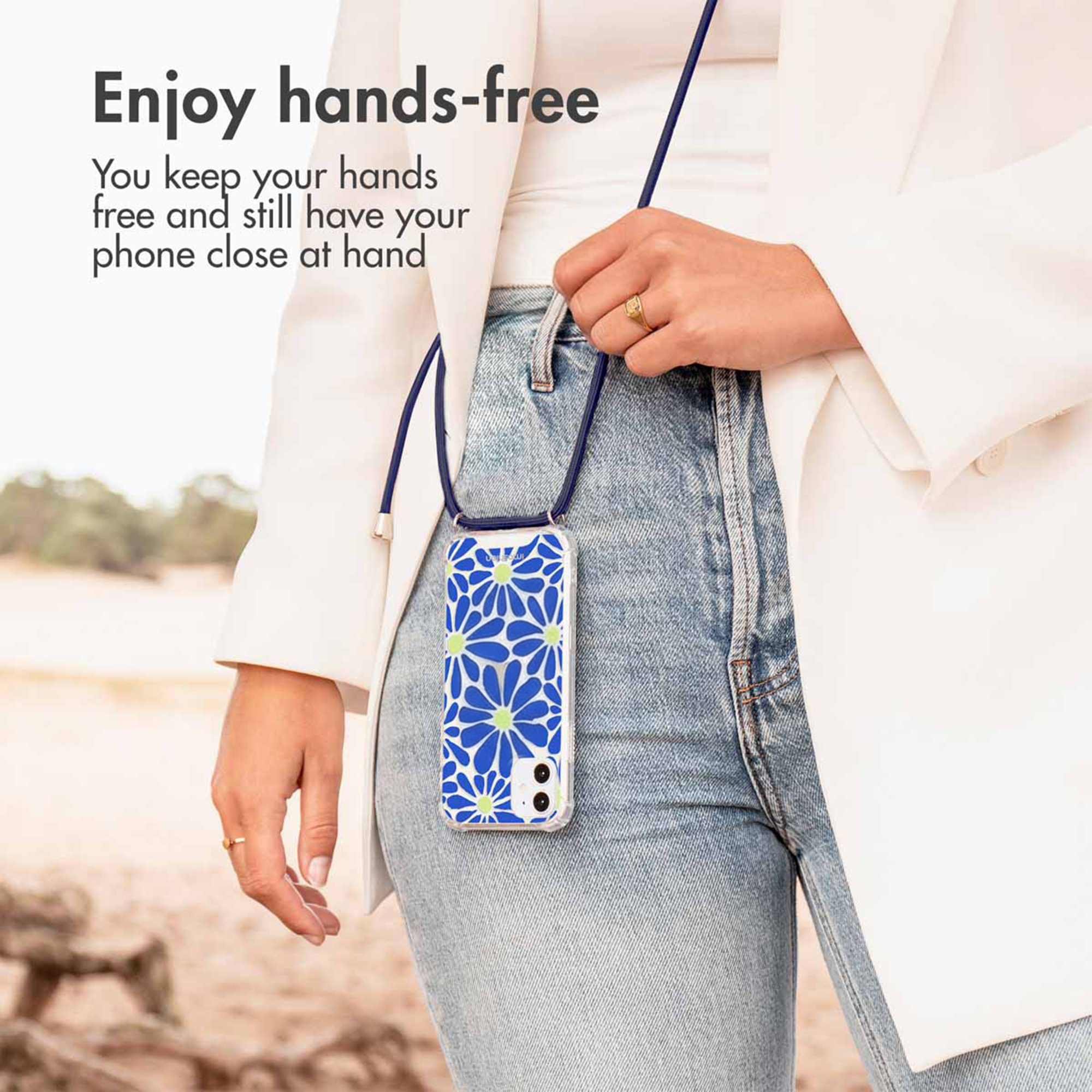 Une femme porte un téléphone à motif bleu et blanc avec cordon bleu sur jean bleu et veste blanche.