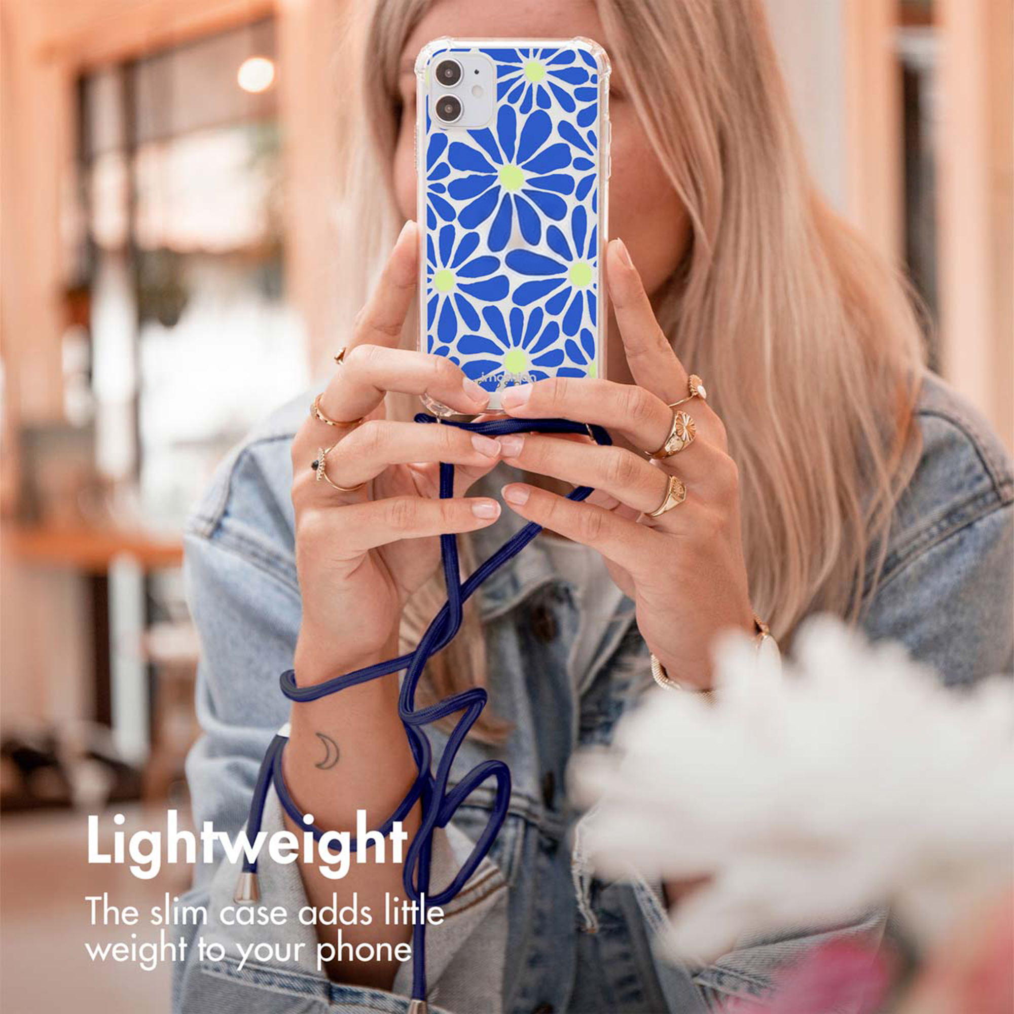 Une femme tient un smartphone avec coque de protection florale et lanière.