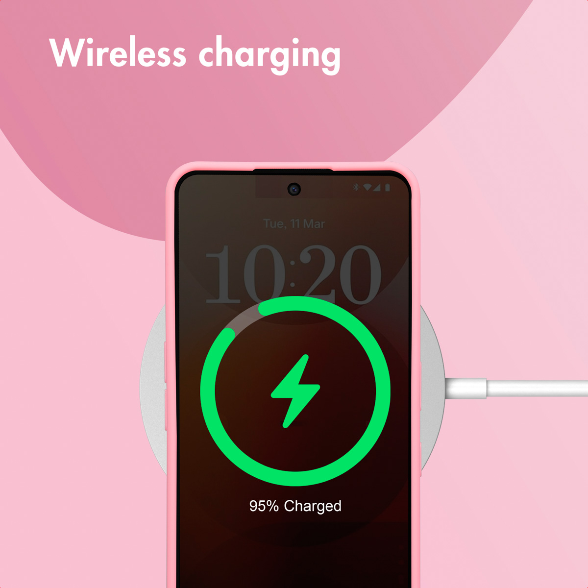 Un teléfono rosa se carga de forma inalámbrica en una base con fondo rosa.