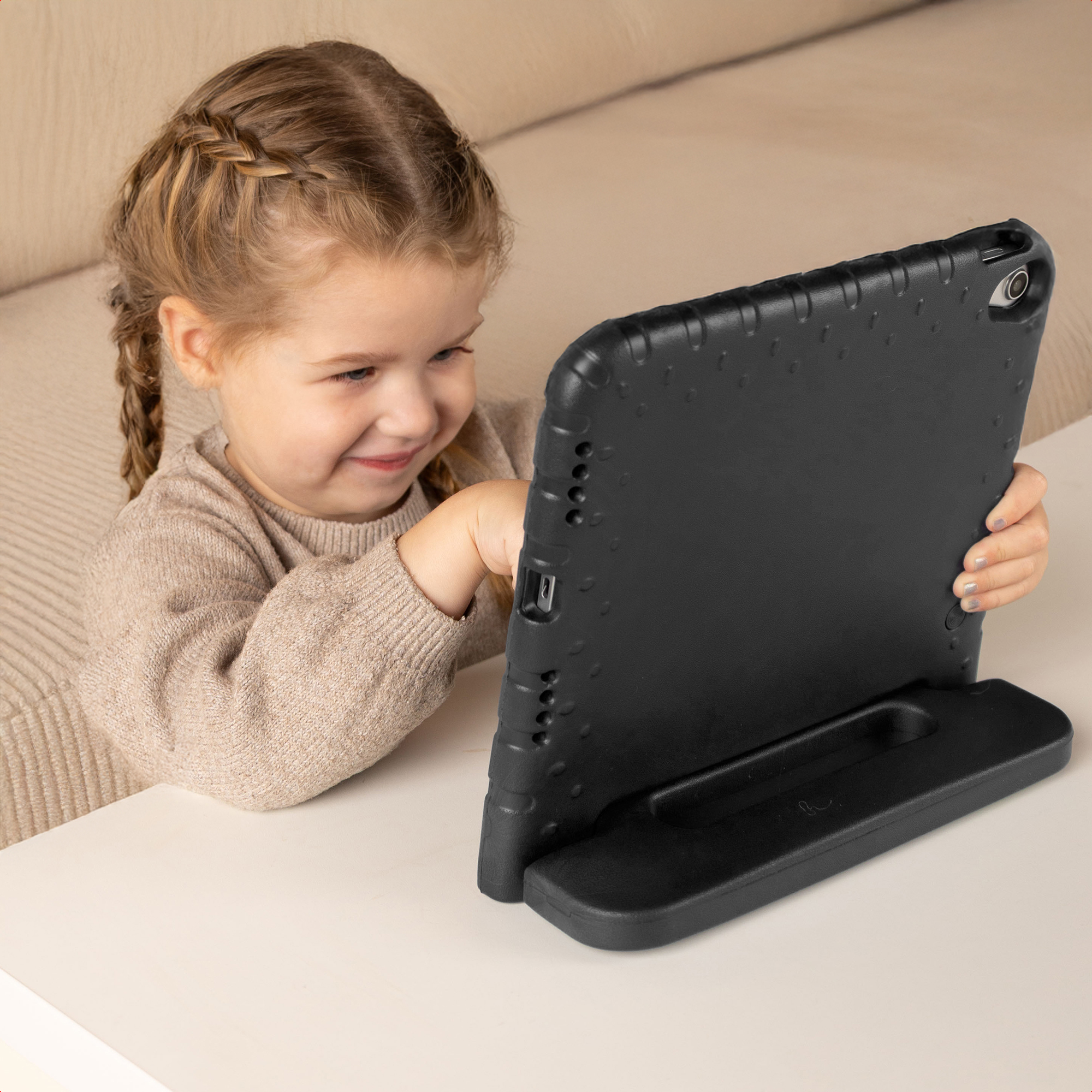 Une jeune fille en pull beige est assise à une table et utilise une tablette dans une coque noire.