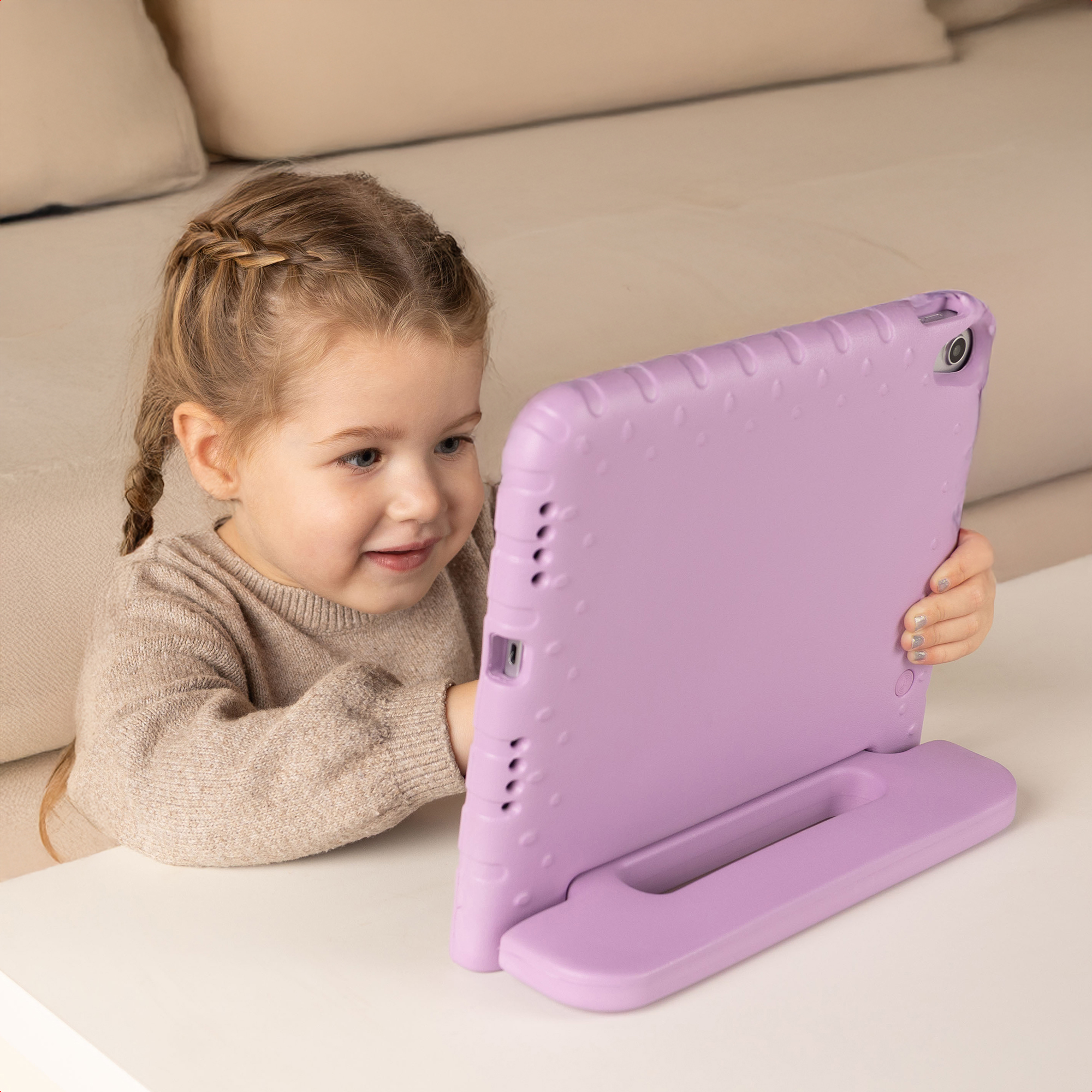 Een jong meisje met gevlochten blond haar glimlacht naar een paarse tablet.