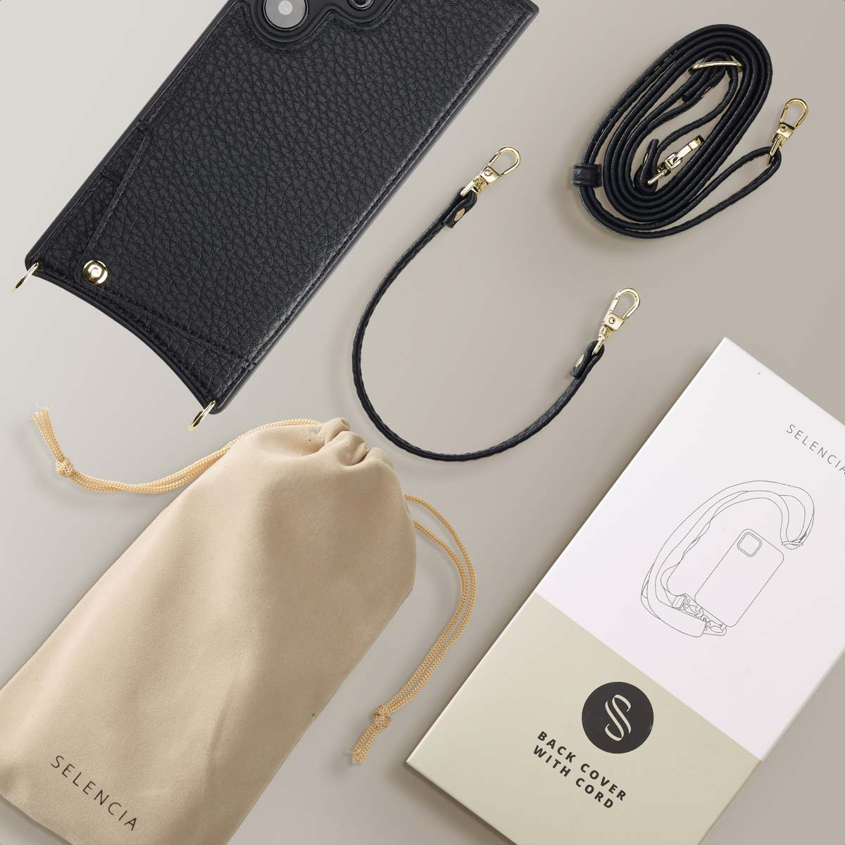 Funda de móvil negra, dos correas negras, una bolsa beis y una caja de producto Selencia sobre fondo beis.