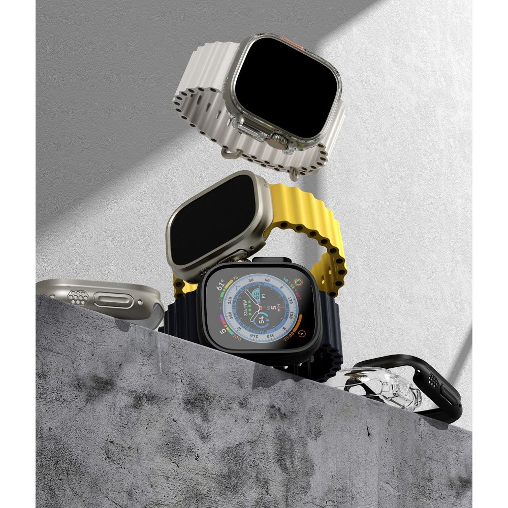 Tre smartwatch con cinturini diversi in bianco, giallo e nero sono disposti su una superficie di cemento.