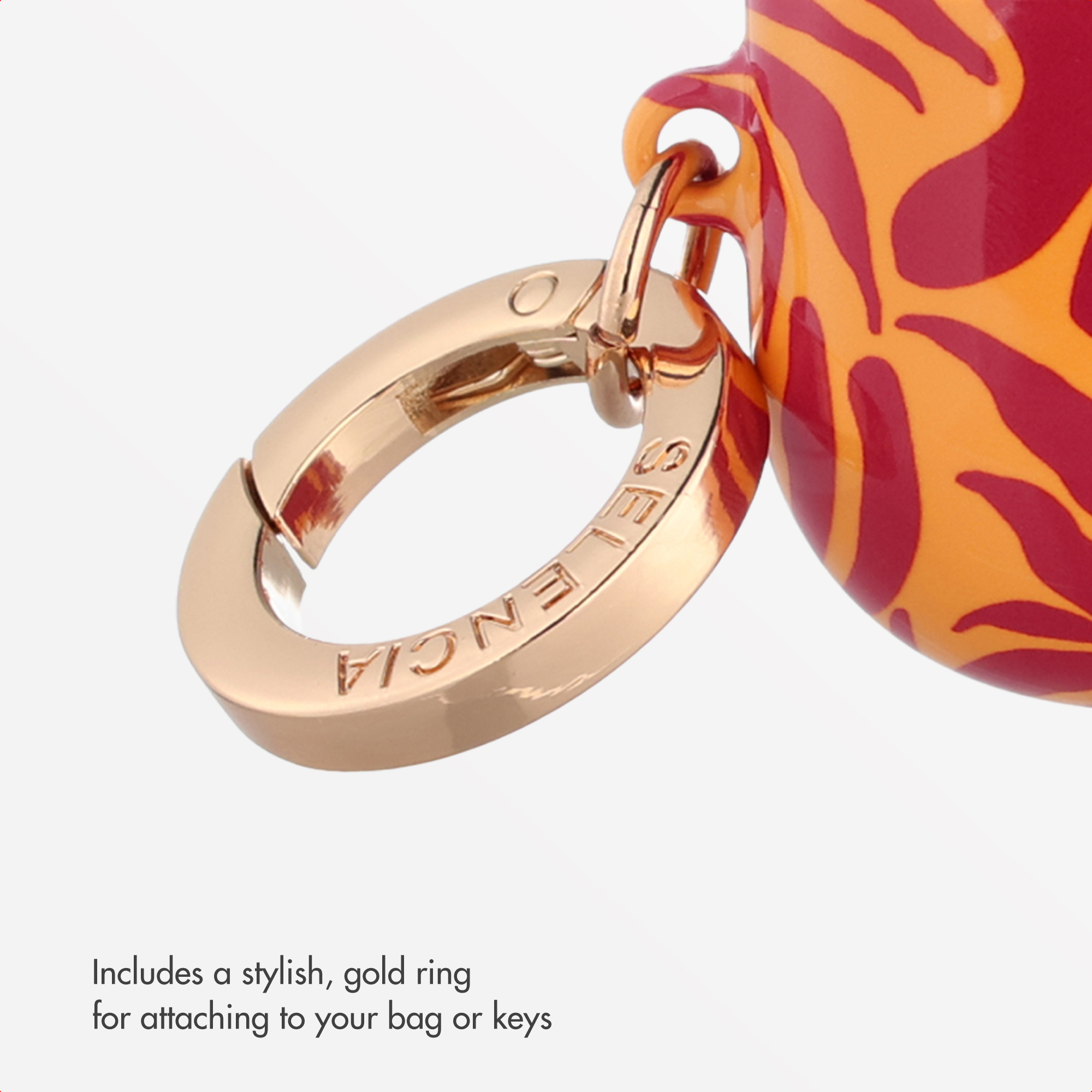 Un anillo dorado unido a un accesorio estampado en rojo y naranja sobre fondo blanco.