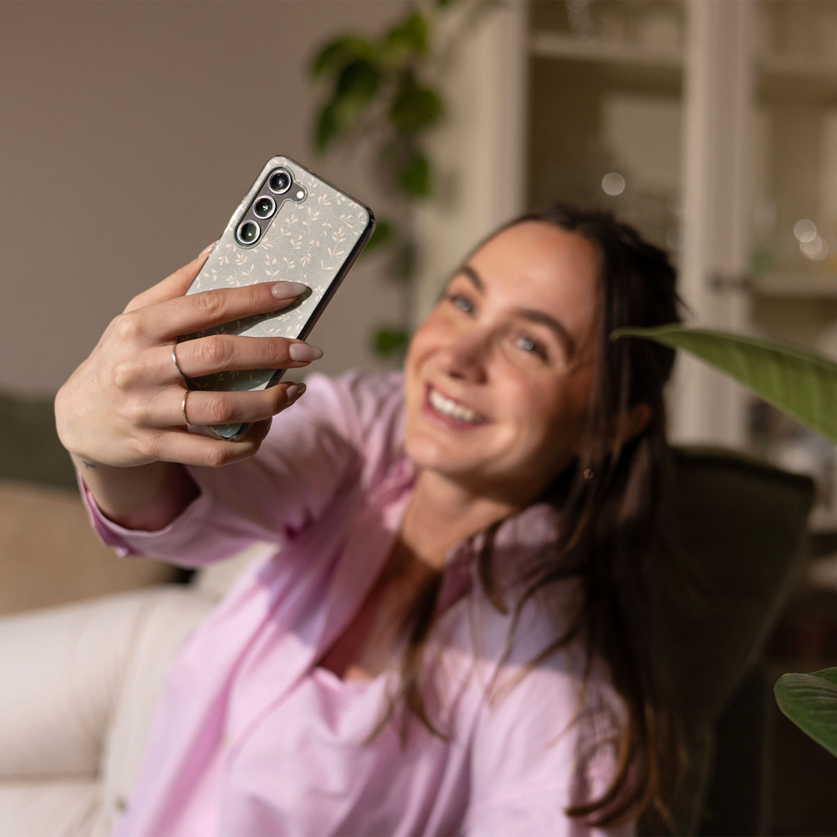 Una mujer sonriente con camisa rosa se toma un selfie con un smartphone estampado.