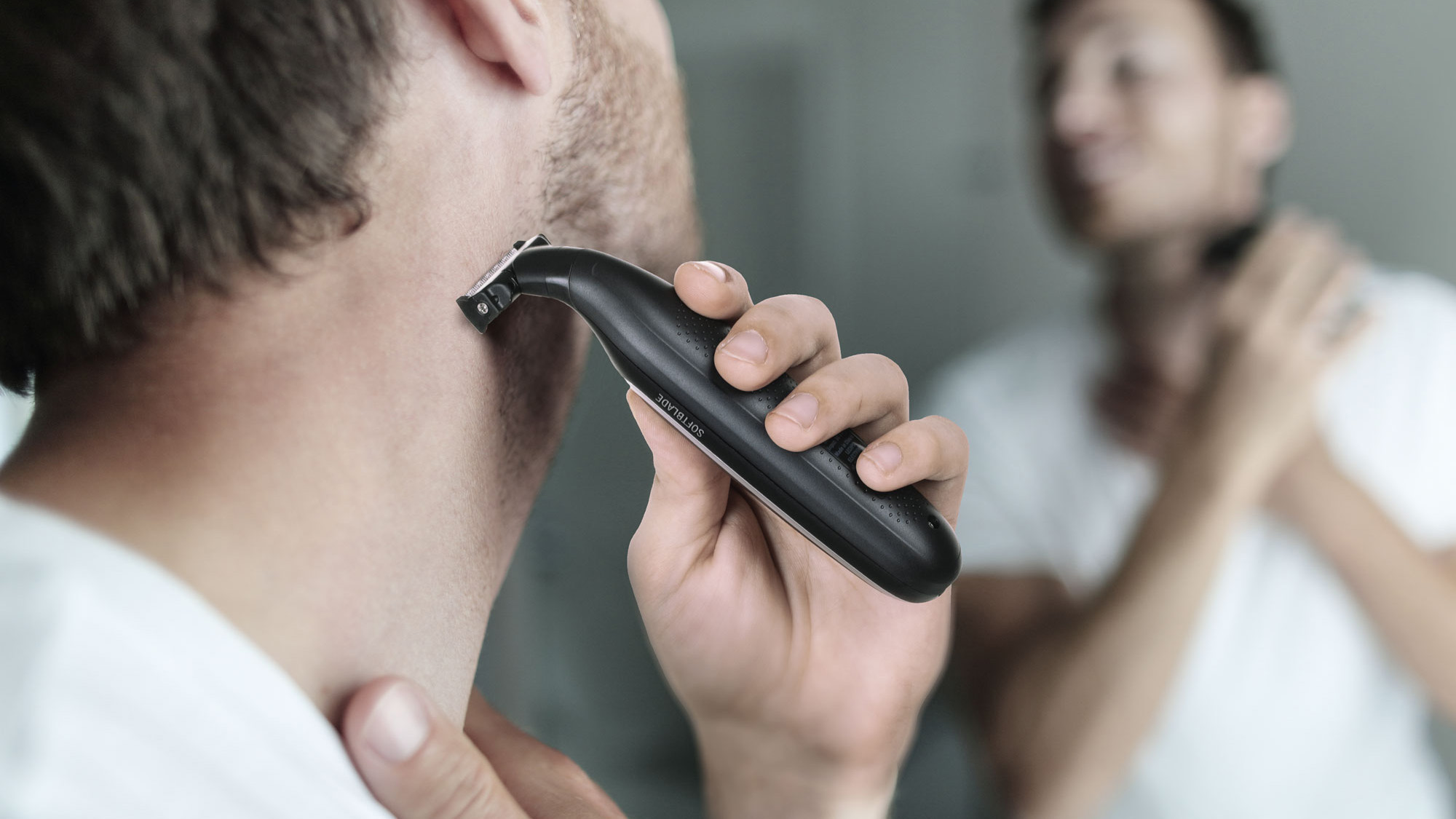 Un uomo usa un rifinitore elettrico nero per radersi la barba, con il suo riflesso visibile nello specchio.