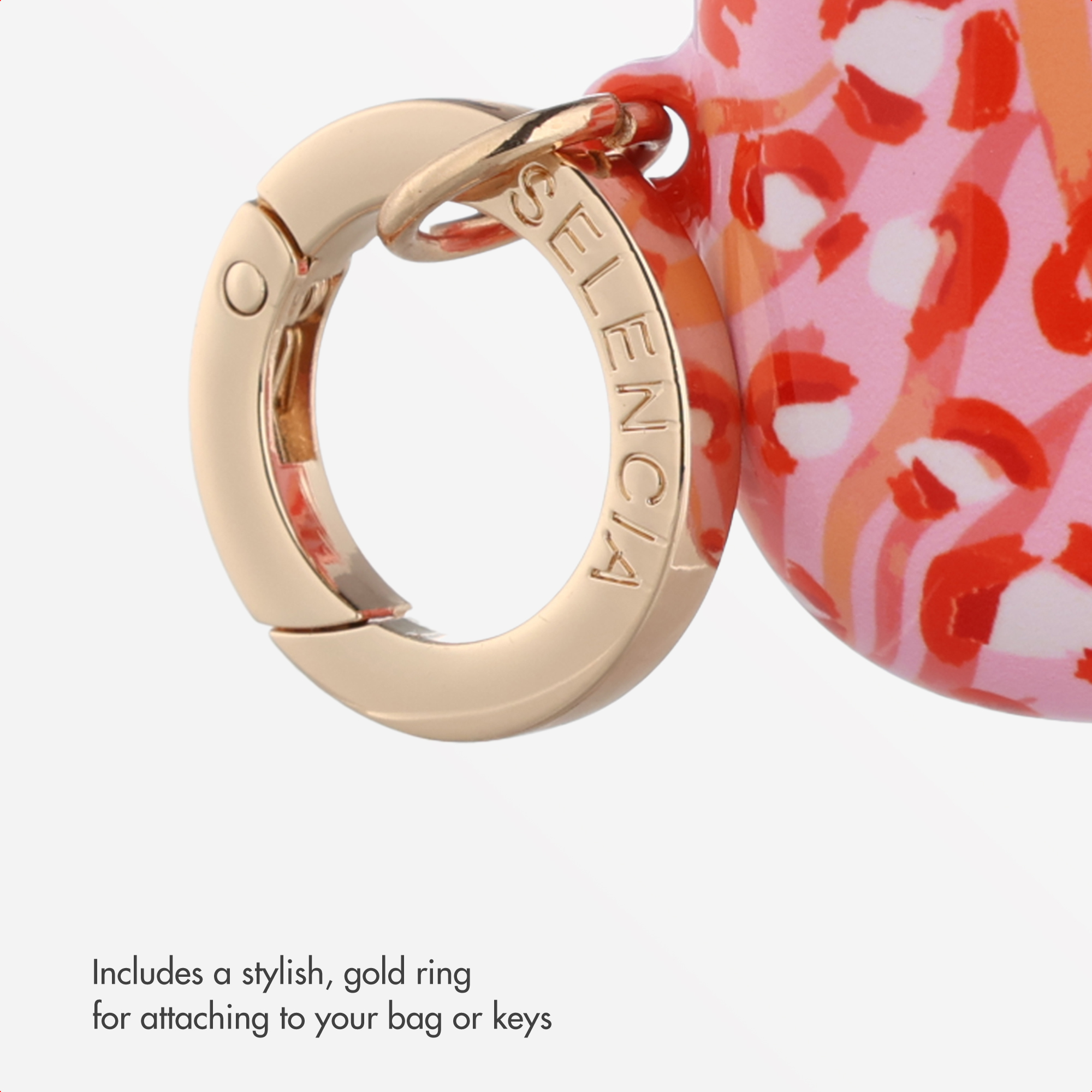 Un anillo de metal dorado con el texto SELENCIA grabado, unido a un objeto con estampado rosa y rojo.