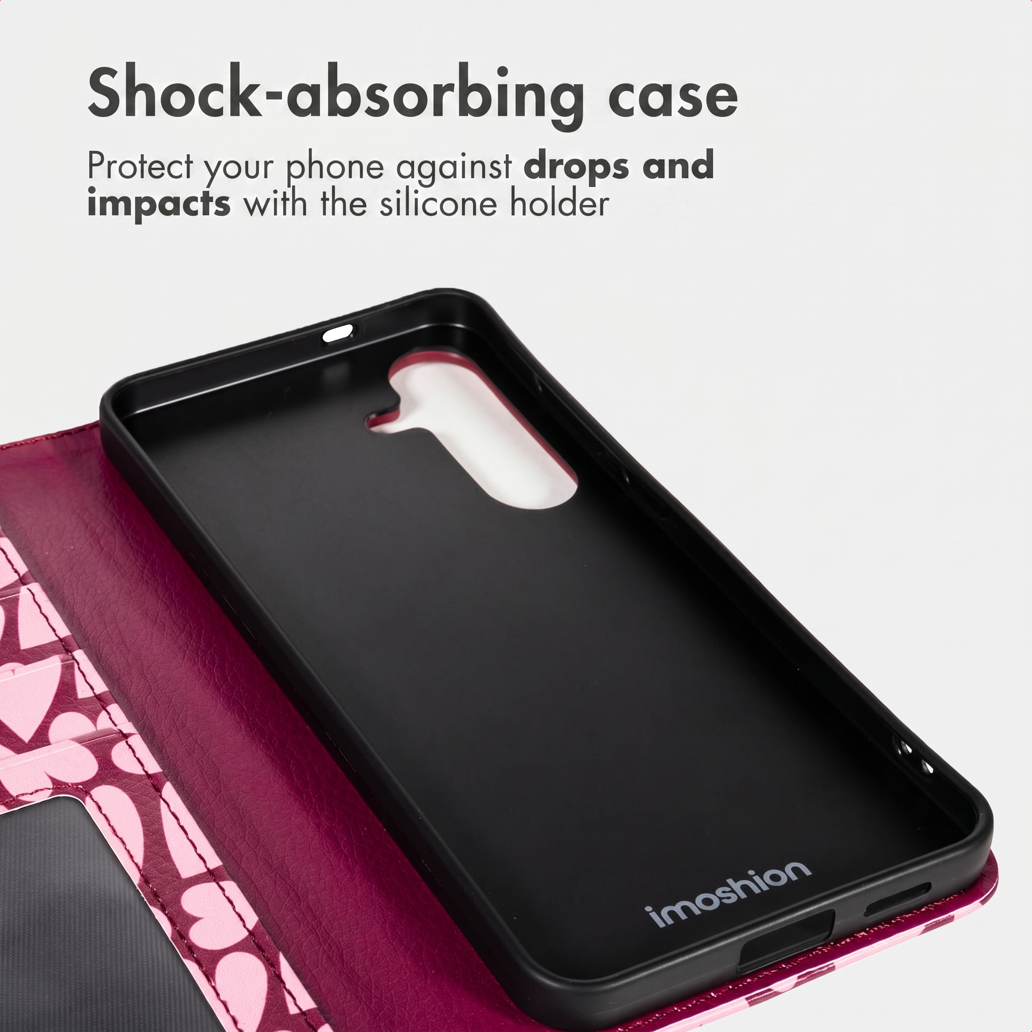 Een roze telefoonhoesje met hartjes en een zwarte siliconen houder binnenin. De tekst luidt Schokabsorberend hoesje.
