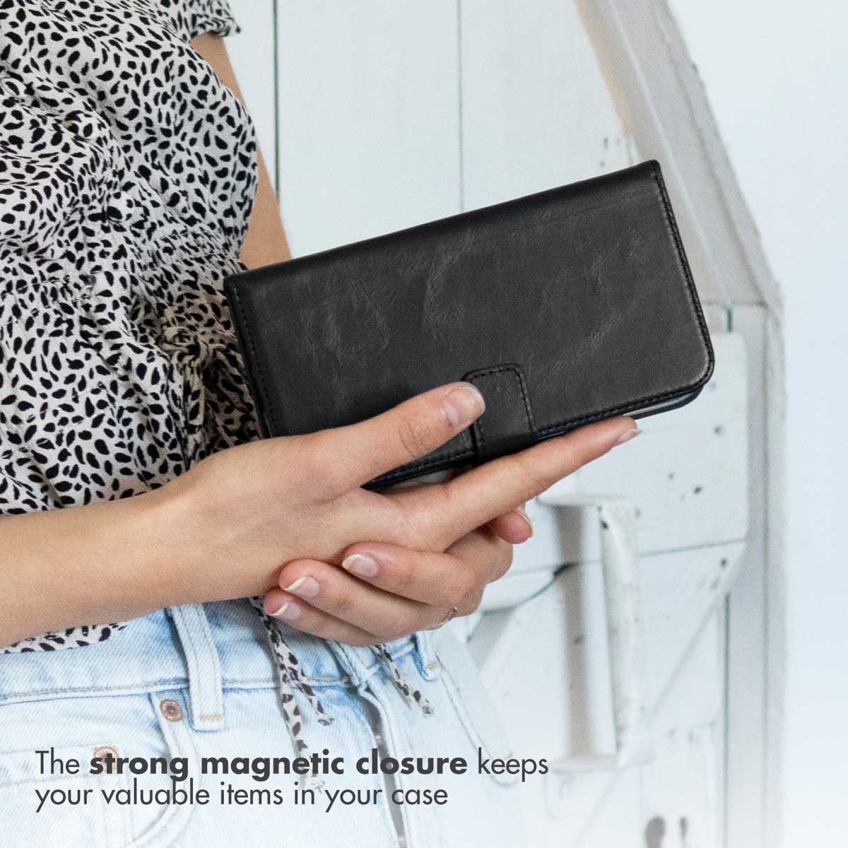 Femme en haut à motif noir et blanc tenant un étui de téléphone en cuir noir sur fond clair.