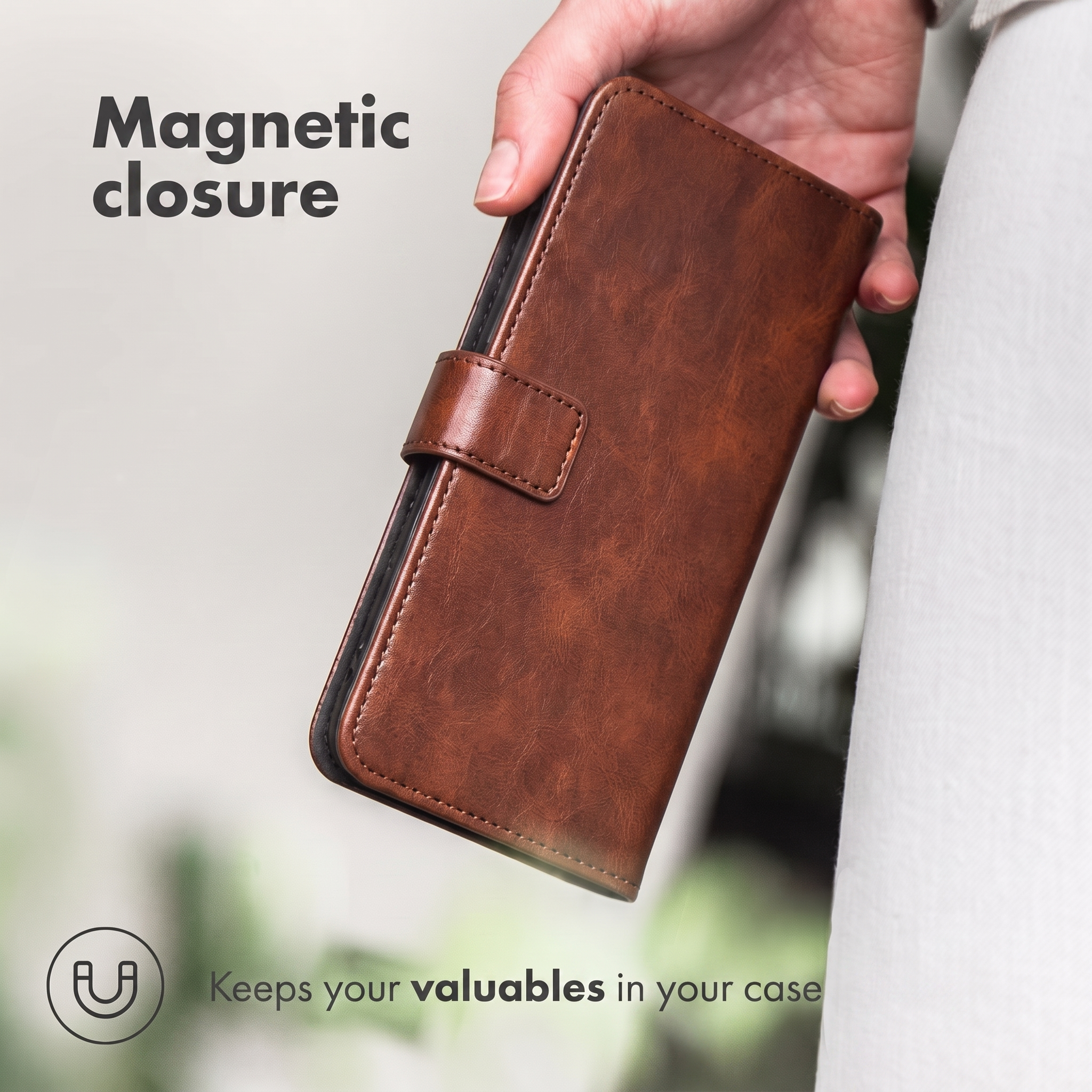 Une main tient un étui de téléphone en cuir marron avec une fermeture magnétique sur fond flou.