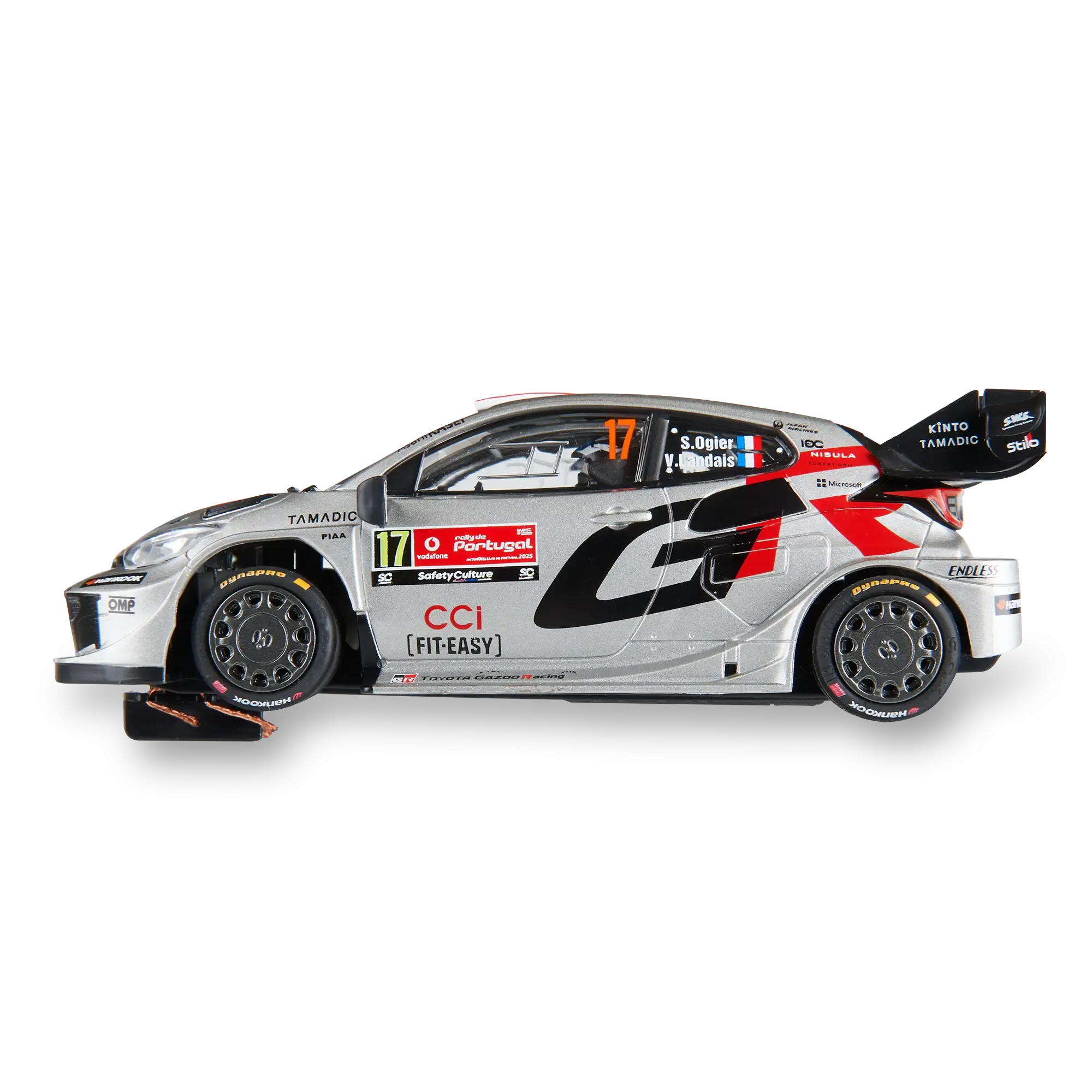 Vista lateral de un coche de rally Toyota WRC plateado con calcomanías de patrocinadores sobre fondo negro.