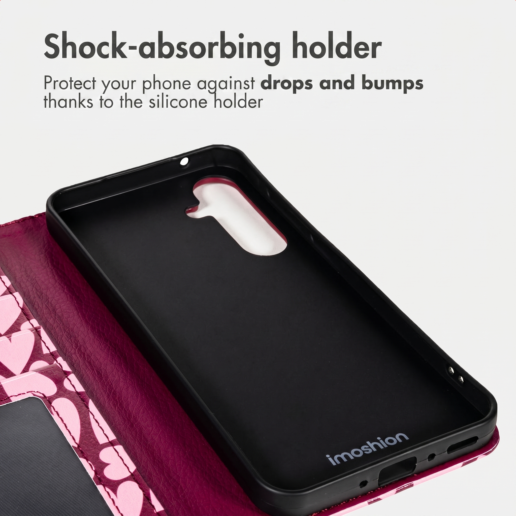 Een roze telefoonhoesje met zwarte siliconen houder en hartjespatroon, met tekst over schokabsorptie.