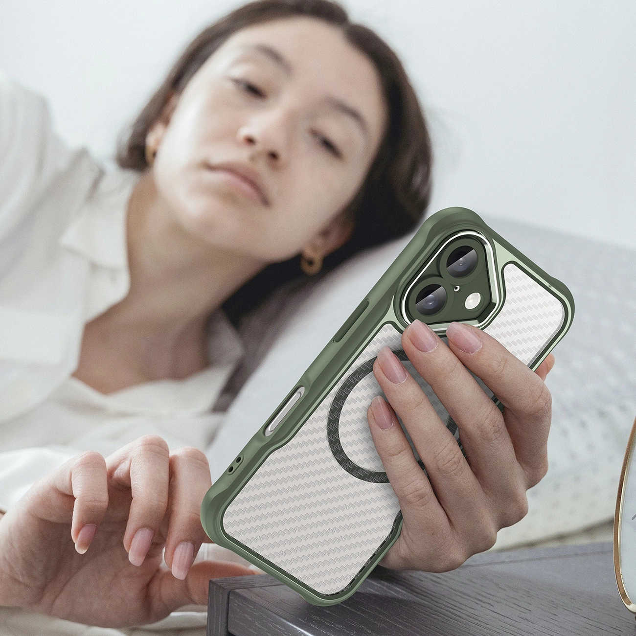Una donna è sdraiata a letto e tiene uno smartphone con custodia verde e retro fantasia.