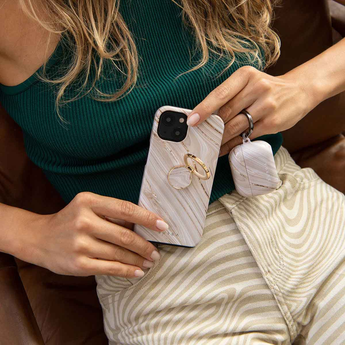 Une femme en haut vert tient un smartphone et un étui assorti au design de marbre blanc avec des touches dorées.
