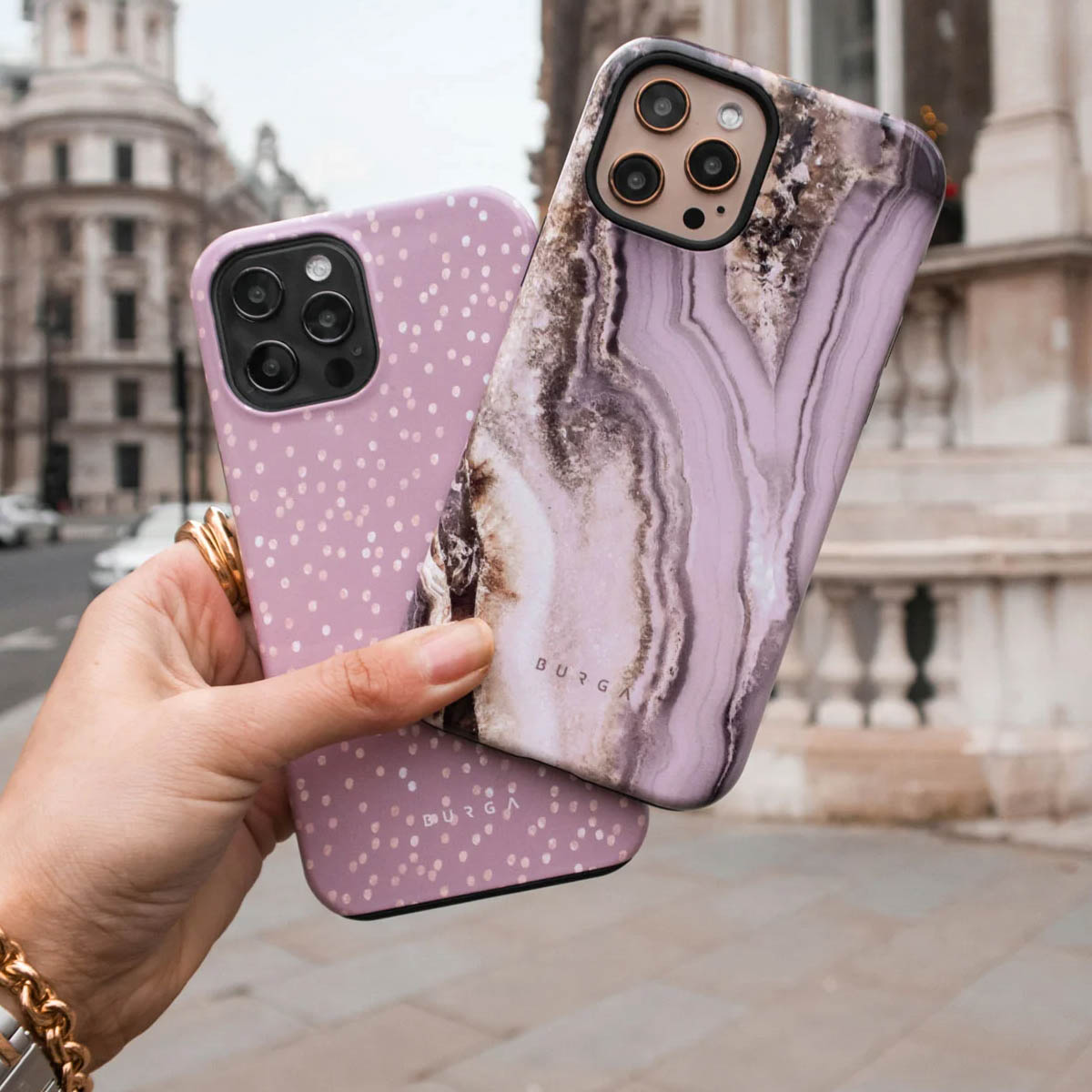 Une main tient deux coques de téléphone violettes devant un fond urbain.