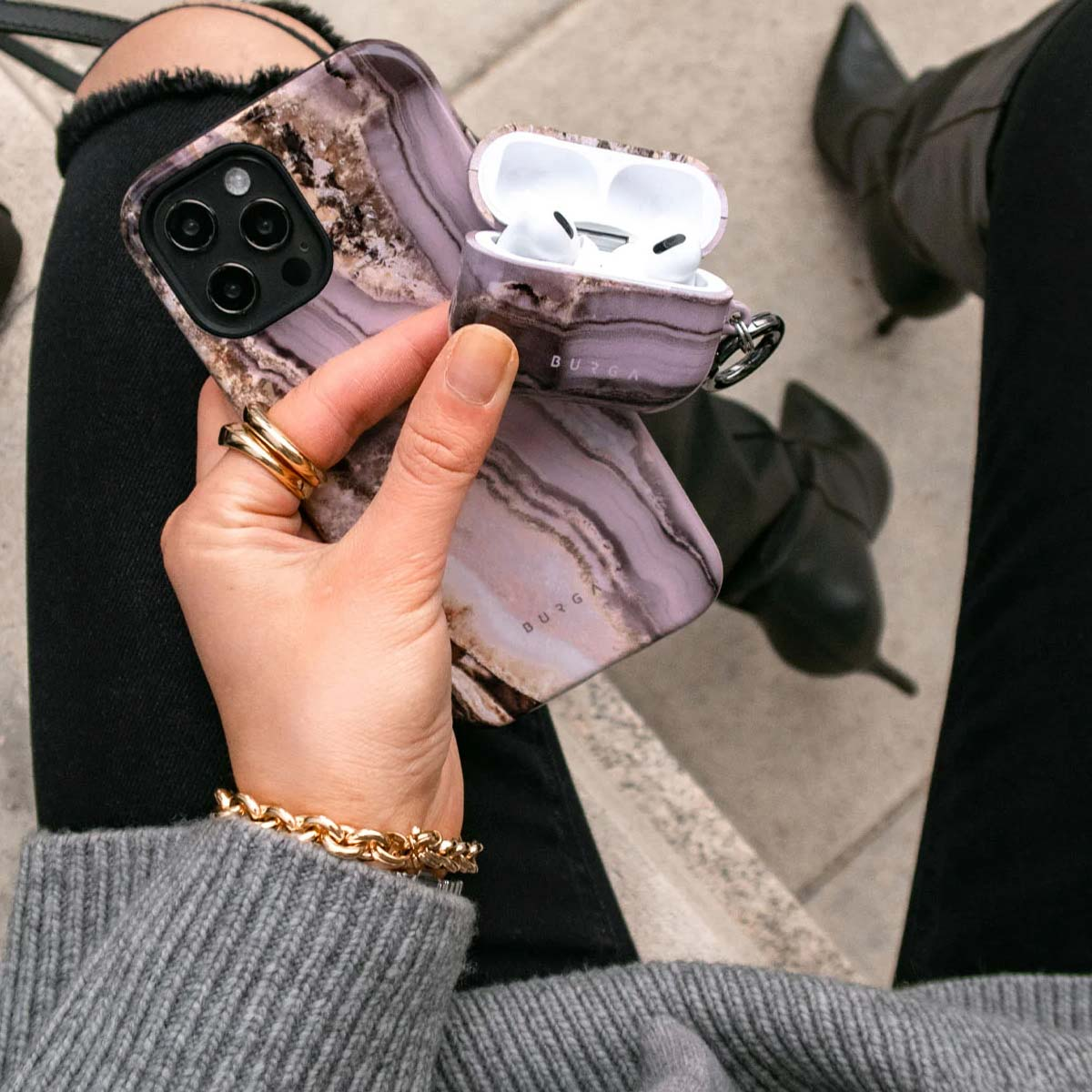Une personne tient une coque de téléphone et d'AirPod en marbre violet assortie, portant un bracelet et des bagues.