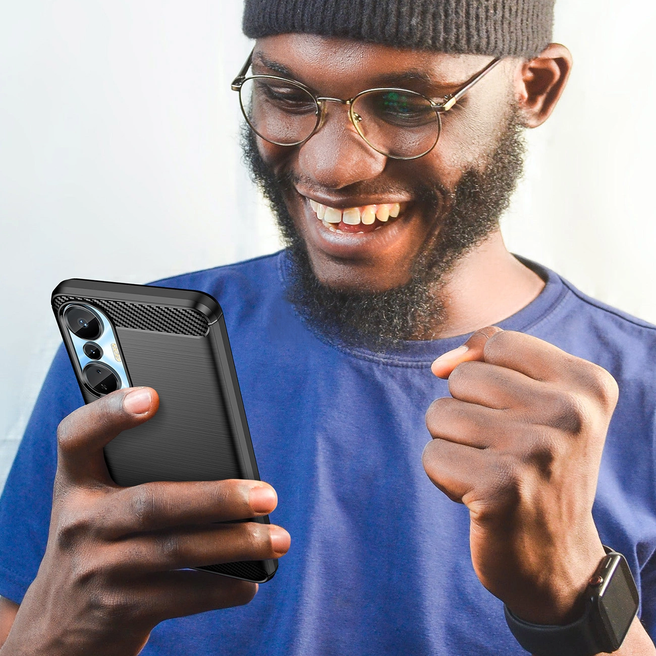 Un uomo felice con camicia blu e berretto tiene in mano uno smartphone nero con custodia.