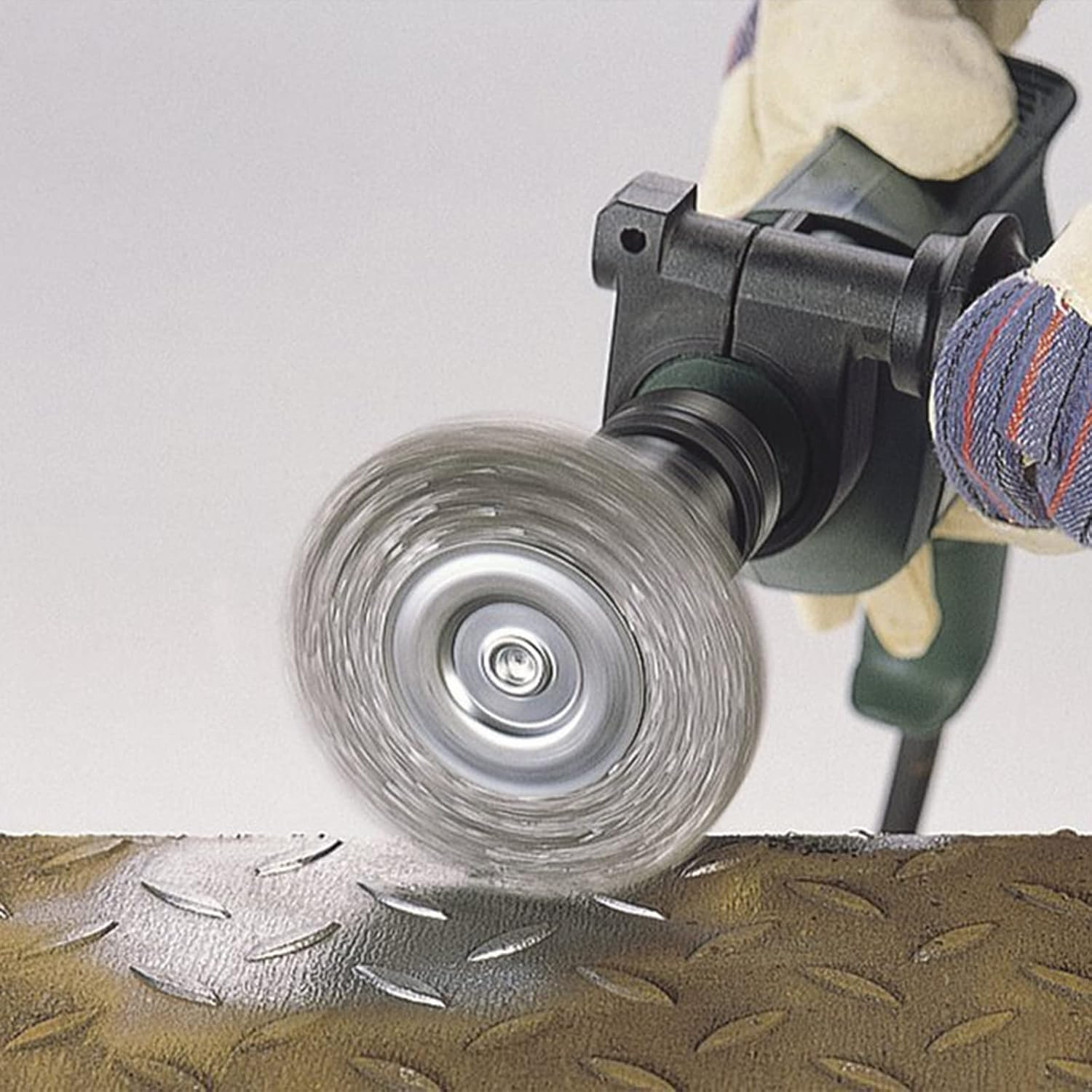 Eine Hand in Schutzhandschuhen hält eine rotierende Drahtbürste, die auf Metalloberflächen arbeitet.