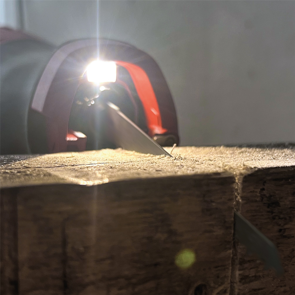 Eine Stichsäge mit heller LED-Beleuchtung schneidet in ein dickes Holzstück, umgeben von Sägemehl.