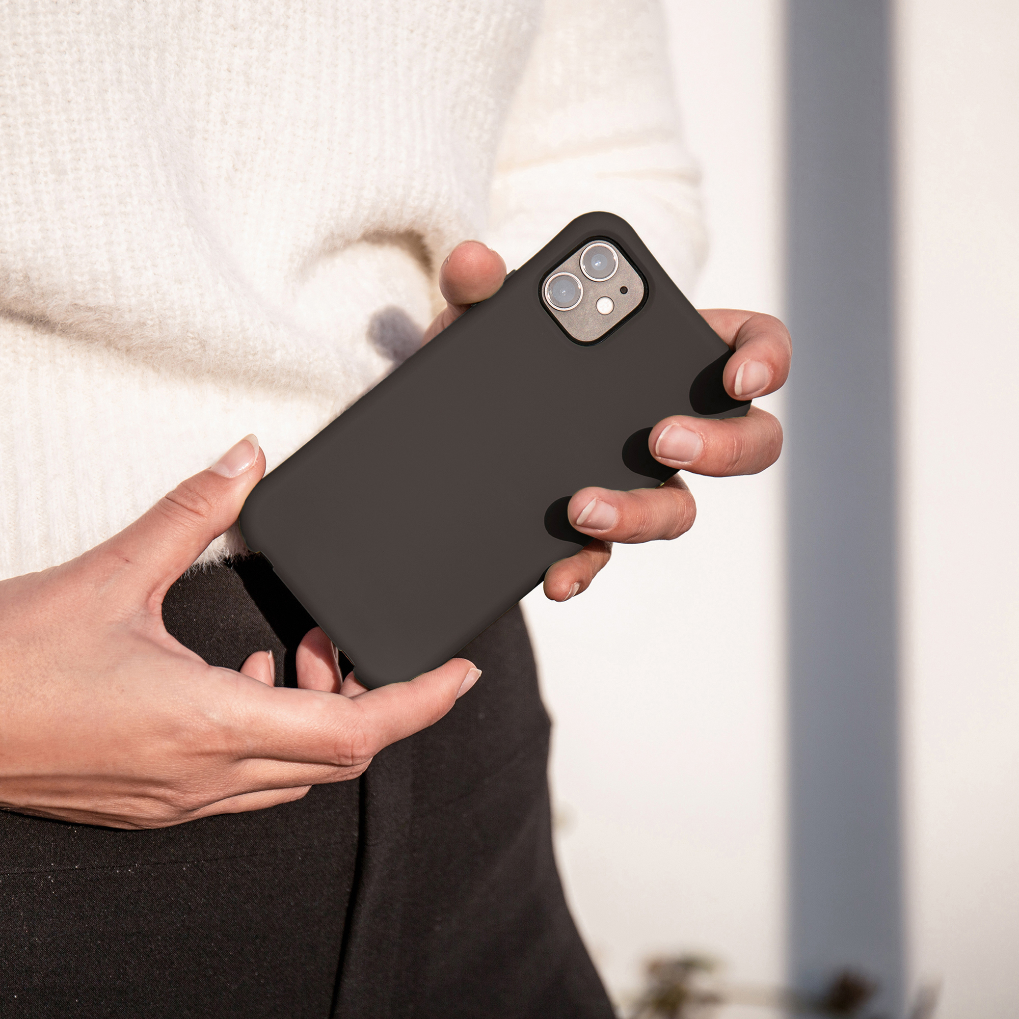 Iemand in een witte trui houdt een zwarte smartphone met dubbele camera vast.