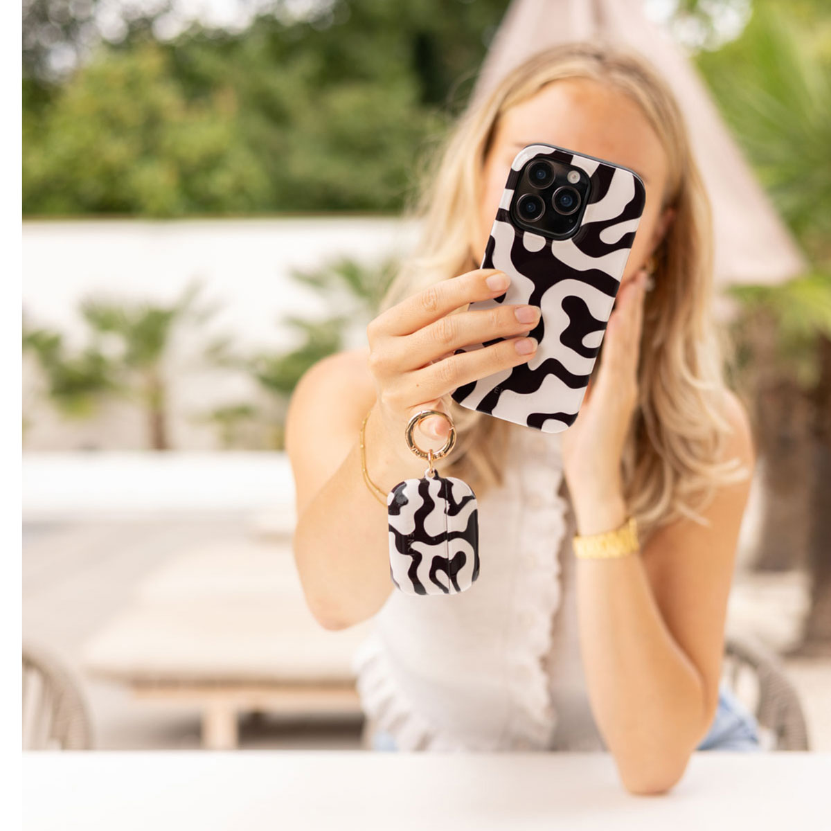 Una donna bionda tiene in mano un telefono con motivo bianco e nero e una custodia coordinata.