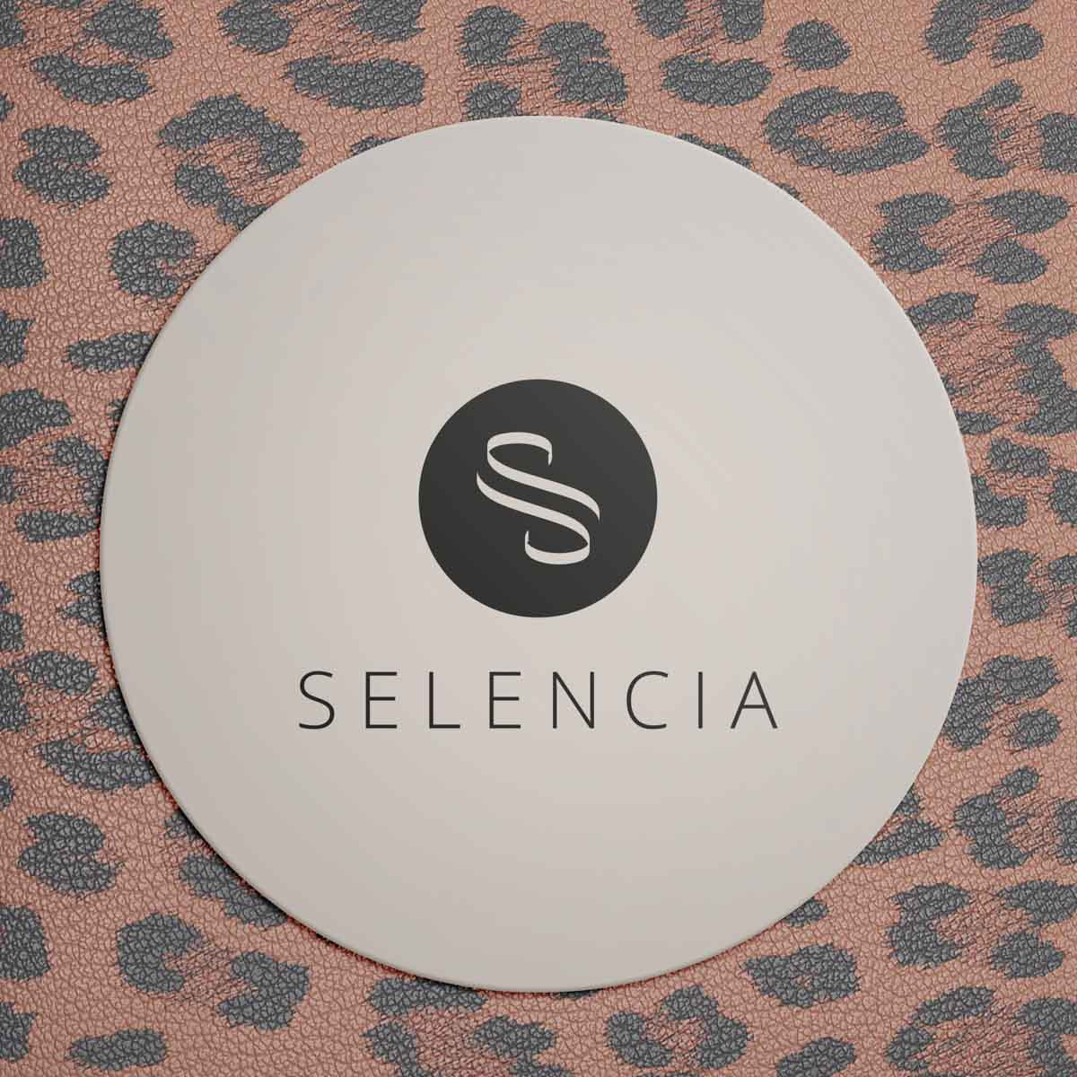 Posavasos redondo blanco con logotipo negro y texto SELENCIA sobre fondo de estampado de leopardo rosa.