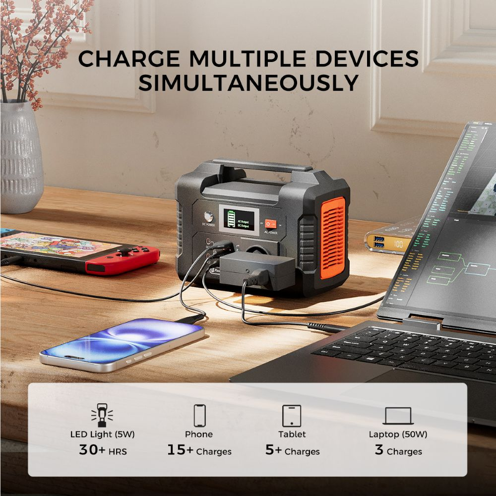 Una estación de energía negra en un escritorio de madera, cargando simultáneamente un teléfono, una laptop y una consola.
